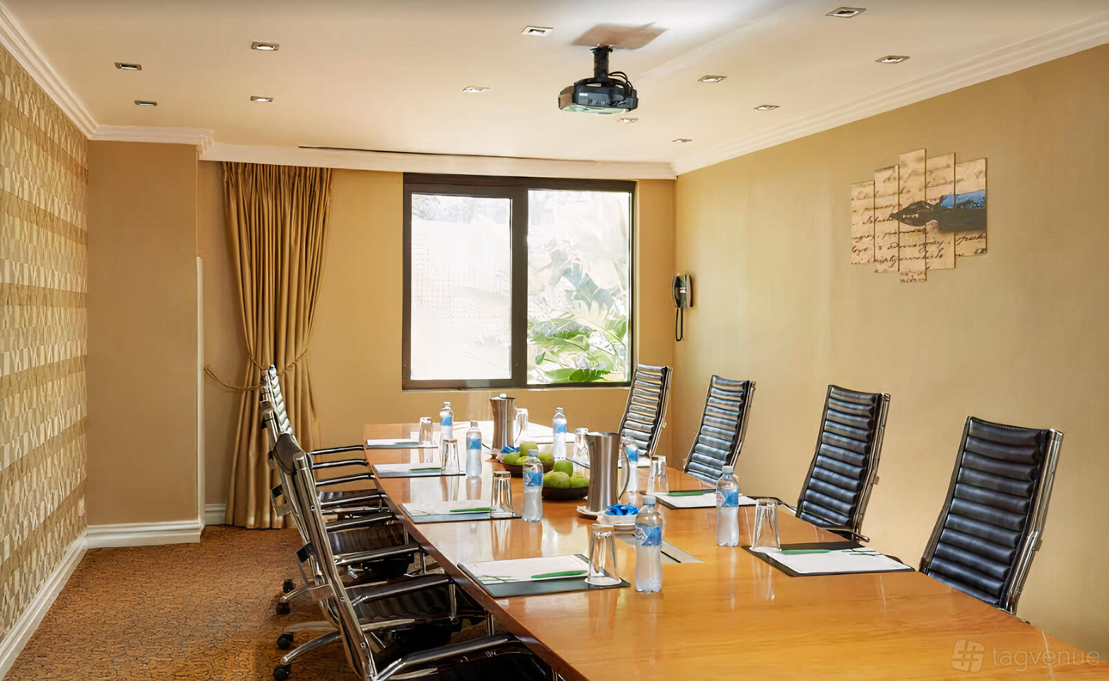 A boardroom with a long wood table, black leather chairs, water bottles, and a ceiling projector at Holiday Inn Parramatta.