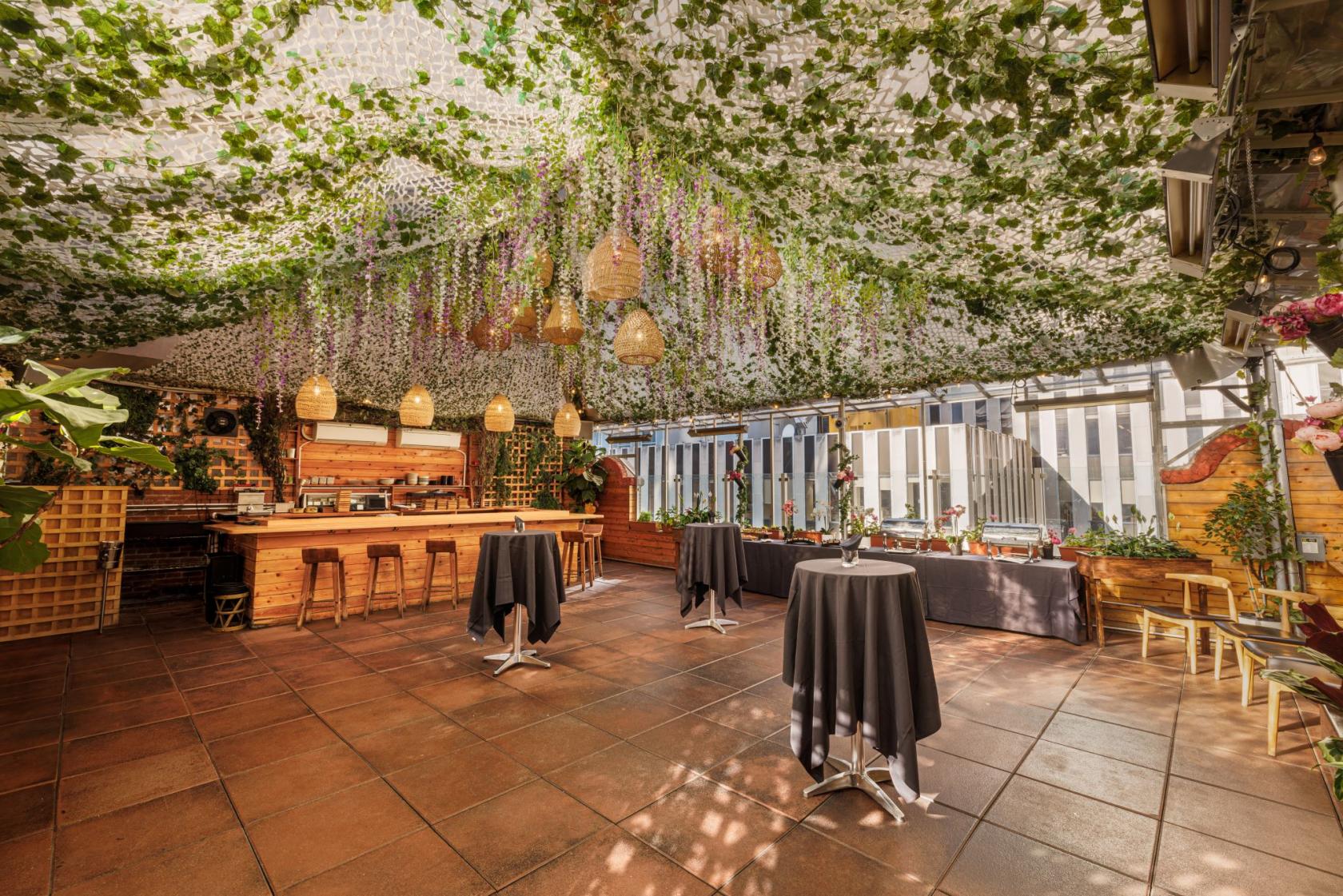 A restaurant with a vine-covered ceiling, hanging wicker lights, and high-top tables with black linens at Sushi Lab.
