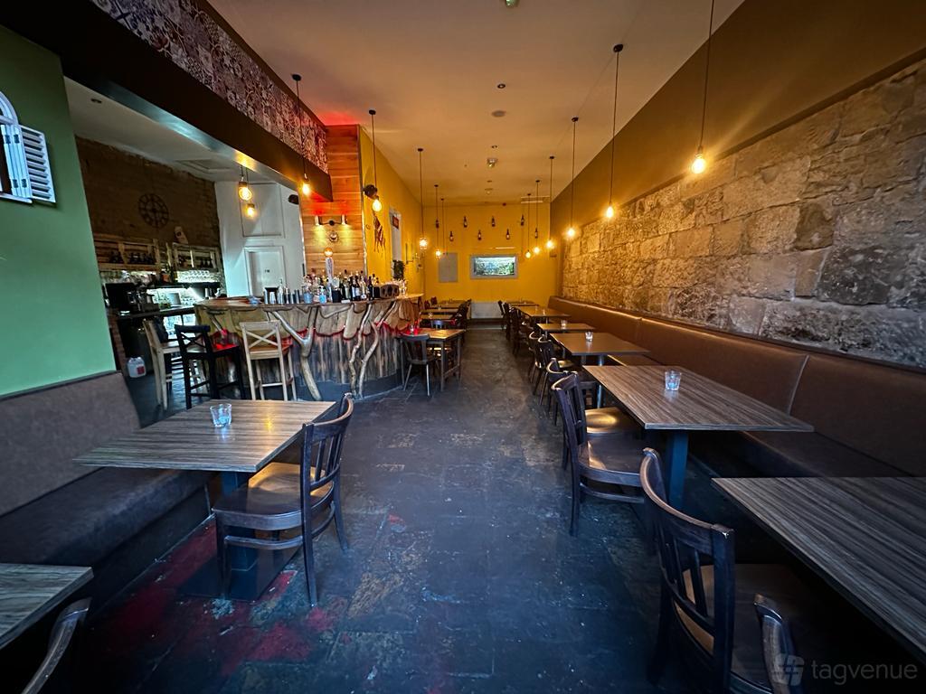 A bar with exposed stone walls, pendant lighting, wooden tables, and a long upholstered bench at 91B Private Venue.