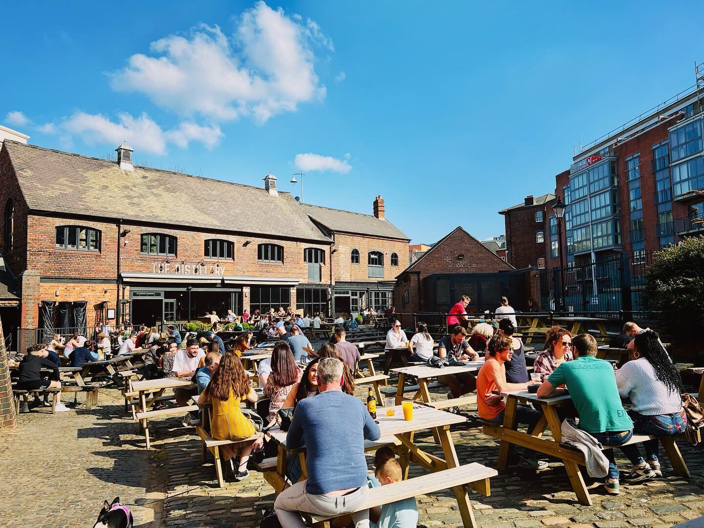 An outdoor bar area with wooden picnic benches on a cobblestone patio at The Distillery.