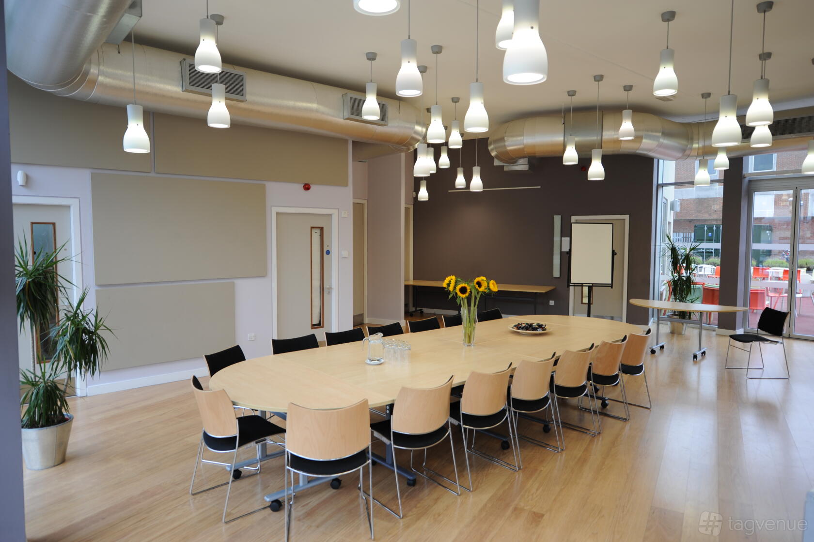 A function room with a large oval table, wooden chairs, pendant lighting, and floor-to-ceiling windows at Signing Tree Venue.