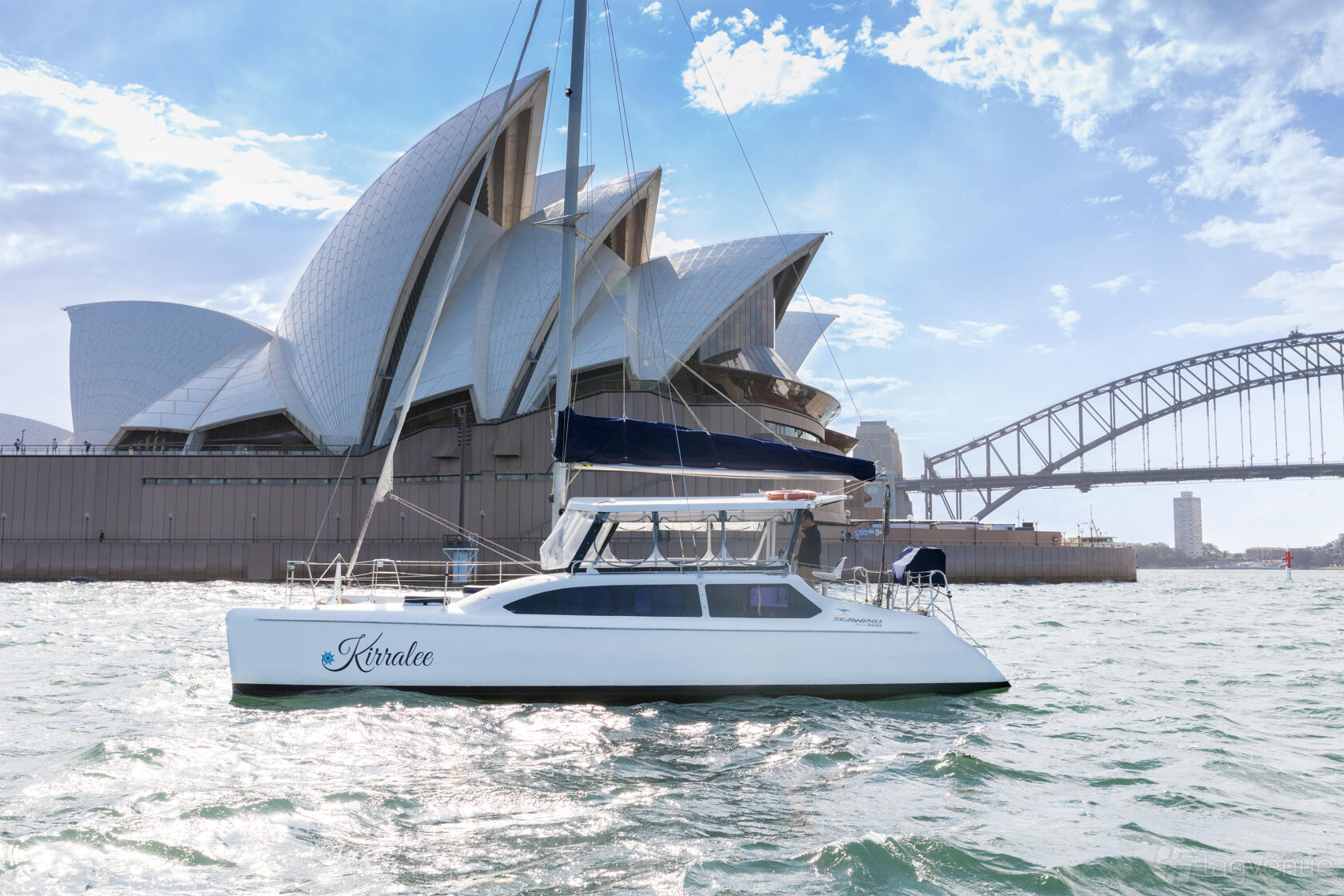 A white catamaran with shaded seating on the water near the Sydney Opera House at Sea Sydney Harbour.