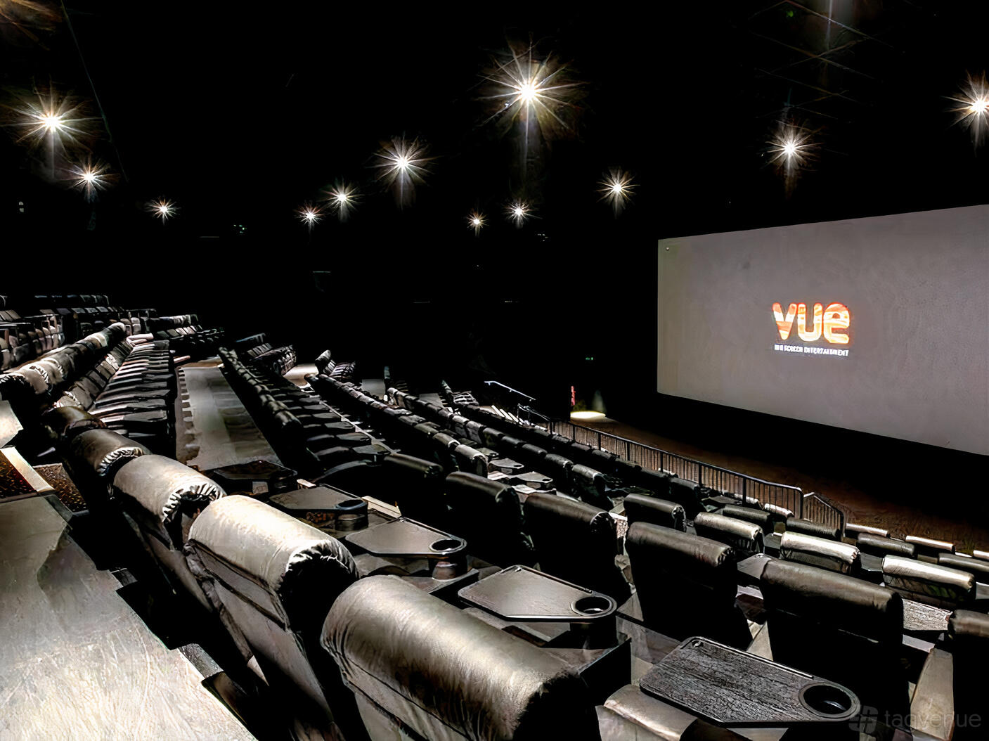 A cinema screening room with tiered rows of black leather recliner seats and a large projection screen at Vue Manchester Quayside.