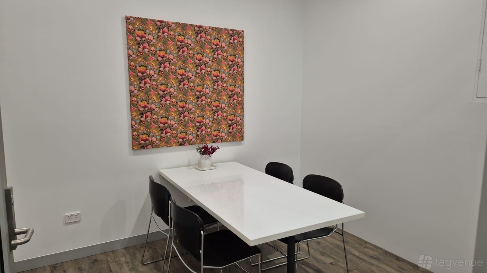 A meeting room with a white rectangular table, black chairs, and floral wall art at Camperdown Quarters.