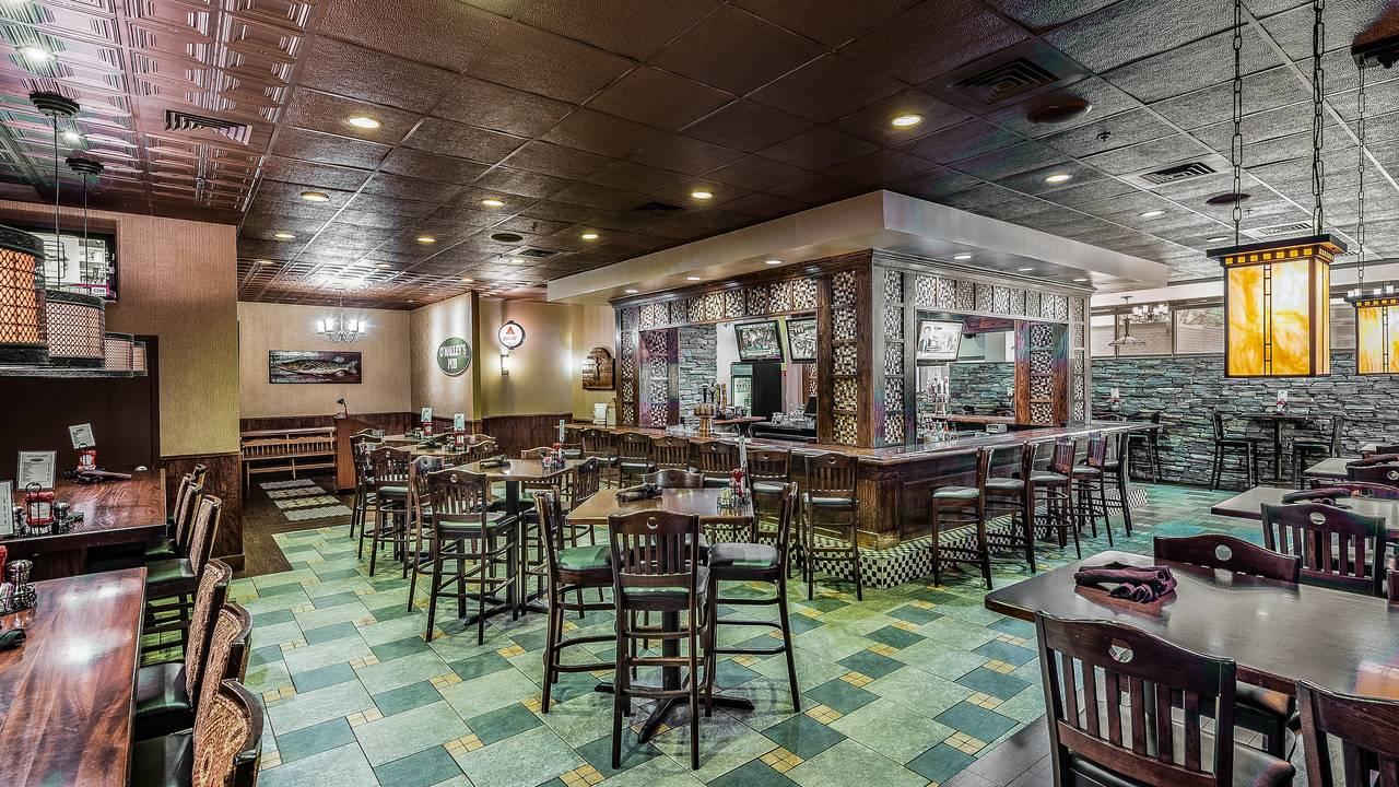 An event space in a restaurant with a central wooden bar, tiled floor, and pub-style tables at O'Malley's - Sterling.