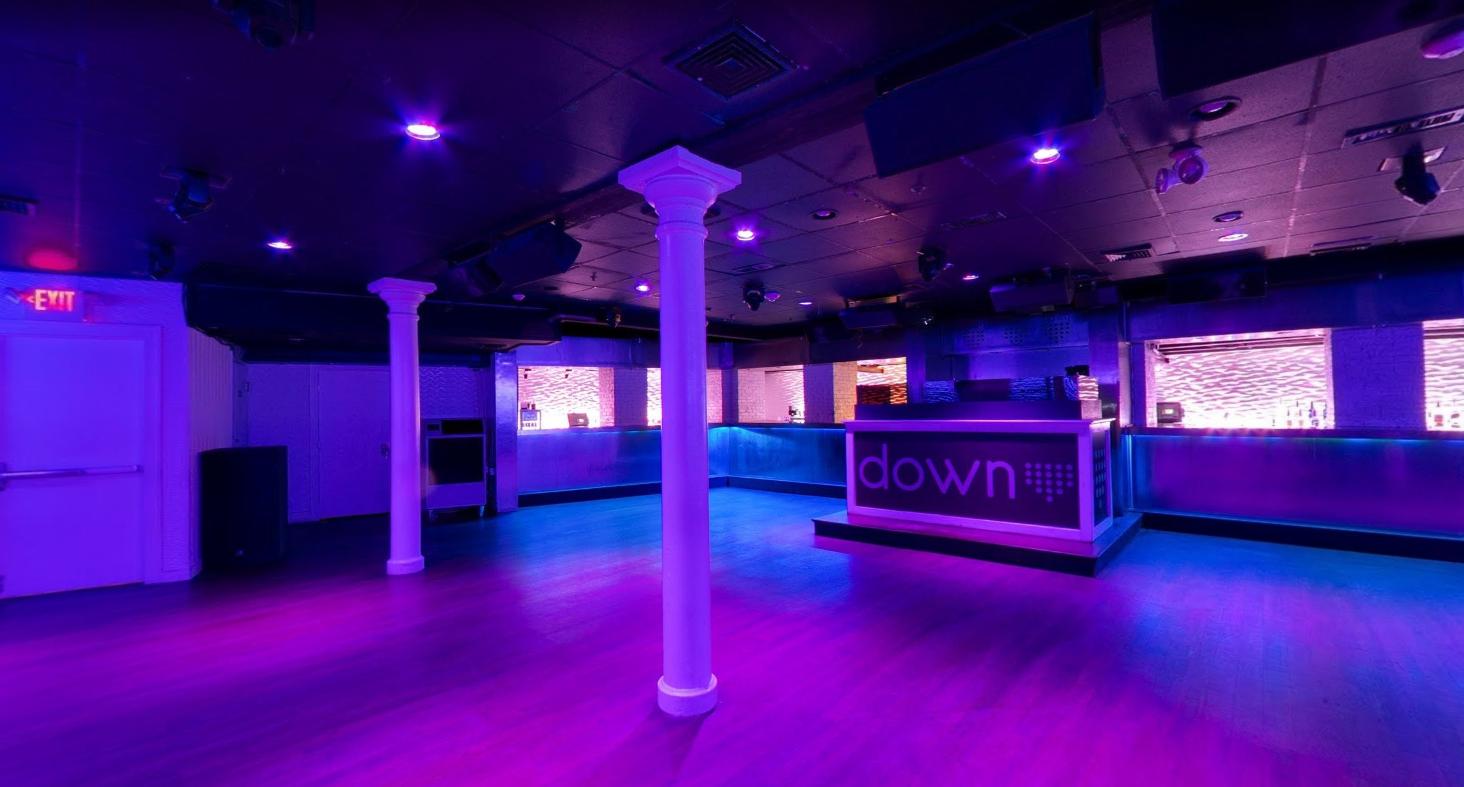An event venue with a dance floor, illuminated columns, and a lit bar counter at DOWN Ultra Lounge, Boston.