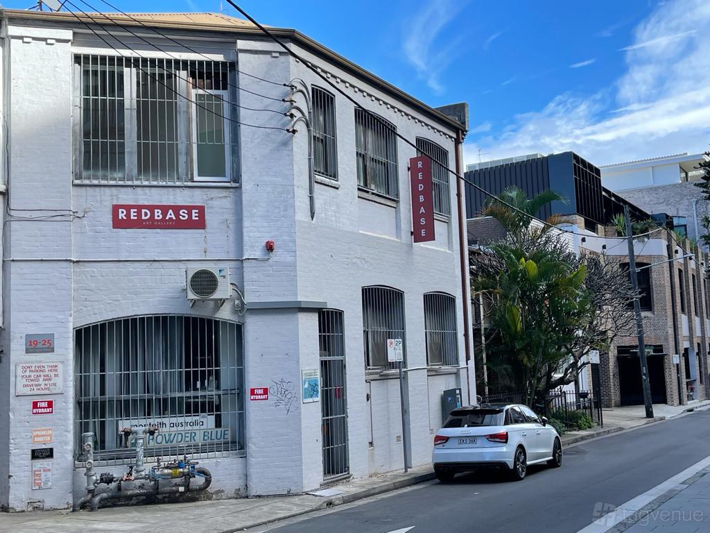 A white brick gallery with large arched windows, metal bars, and a street entrance at Exhibition space @Chippendale.