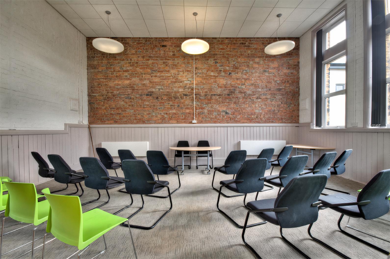 An event space with exposed brick walls, large windows, and rows of black chairs at Heart Centre.
