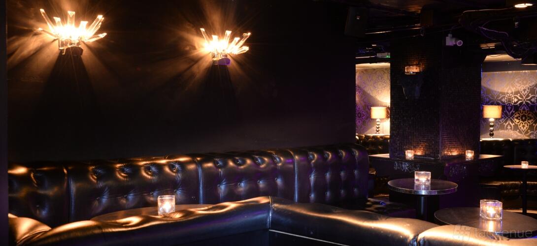 An event space in a nightclub with tufted black leather seating, candlelit tables, and decorative wall lighting at LUXE.