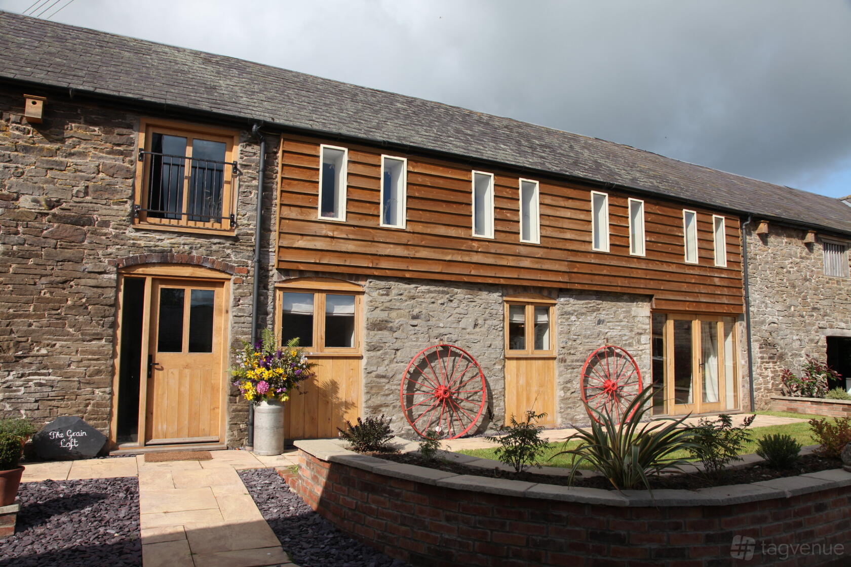 A barn venue with stone walls, wooden accents, red wagon wheels, and large wooden doors at The Grain Loft.
