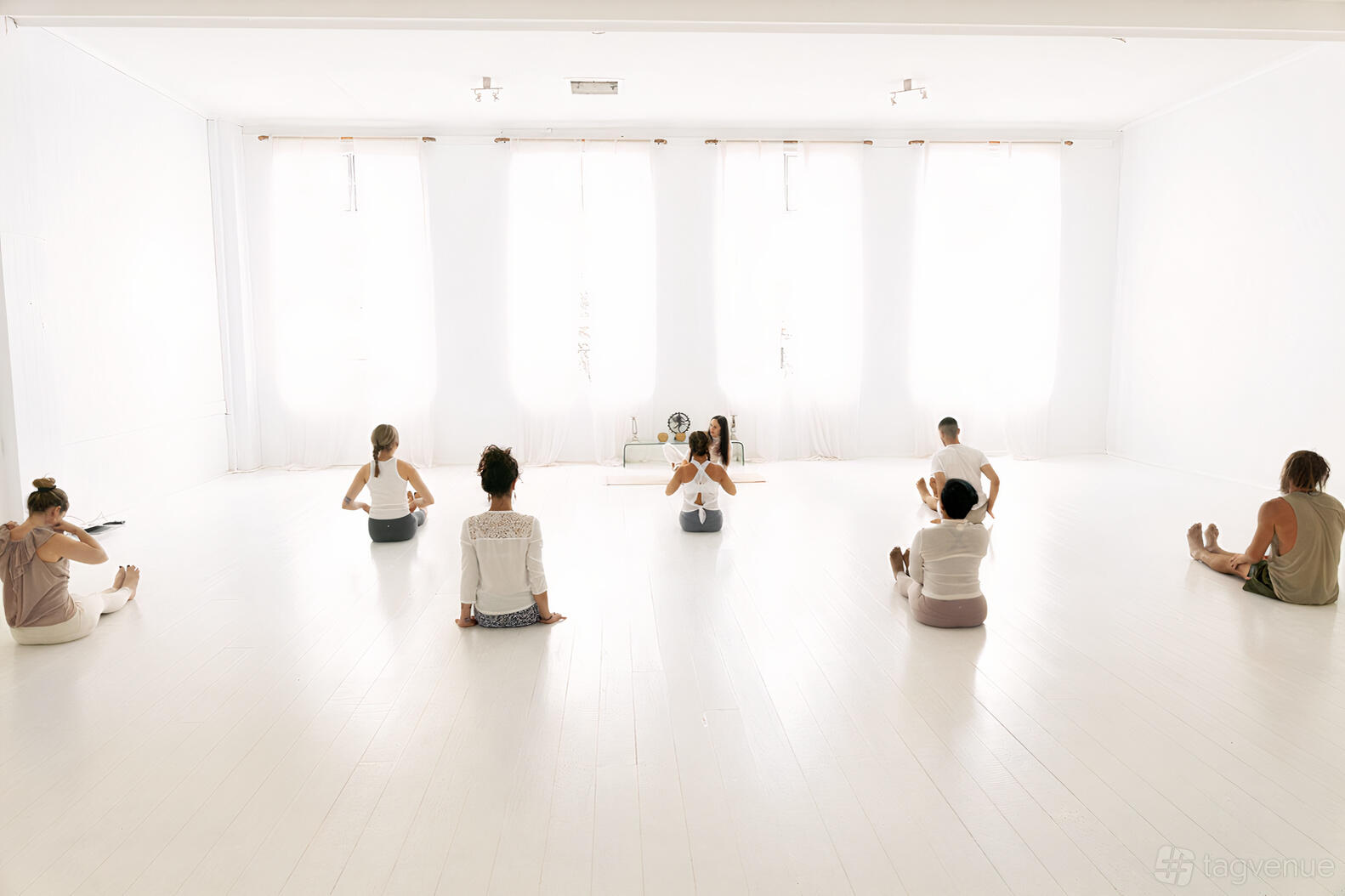 An event venue with a bright white studio, sheer curtains, and a group seated on a polished floor at Prana House.