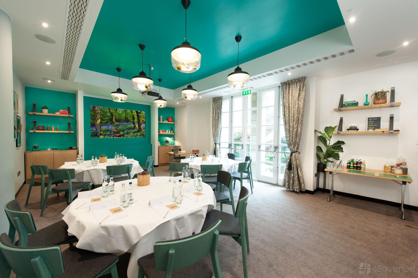 A hotel meeting room with round tables, green accents, and large windows at DoubleTree by Hilton London Kensington.