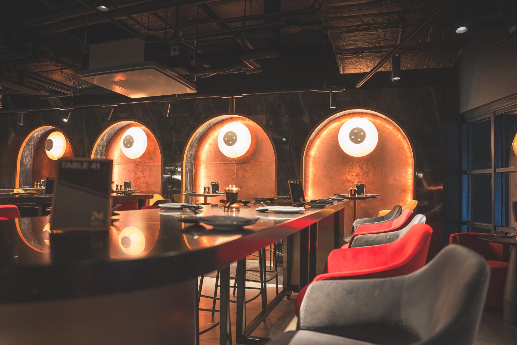 An event venue with illuminated circular wall alcoves, high tables, and red and gray chairs at AO Arena Manchester.