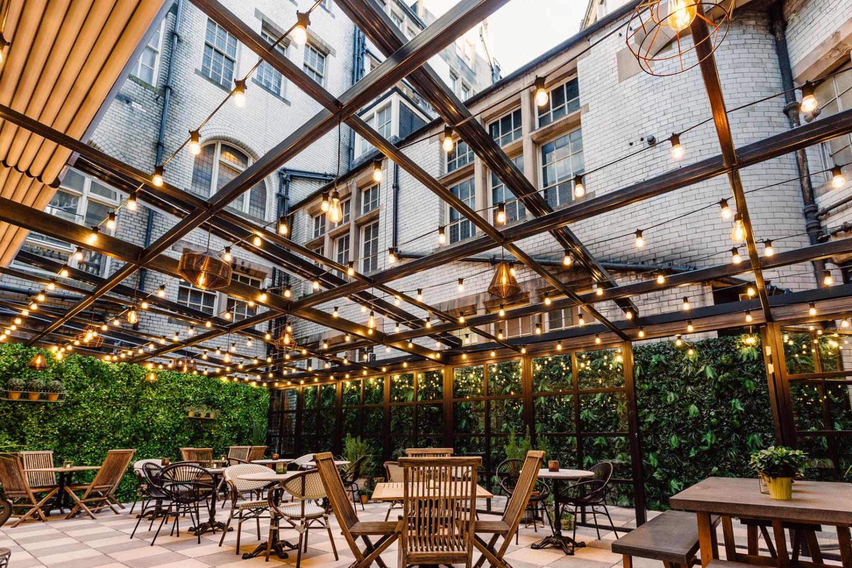 A hotel terrace with checkered flooring, string lights overhead, and wooden tables and chairs at The Scotsman Hotel.