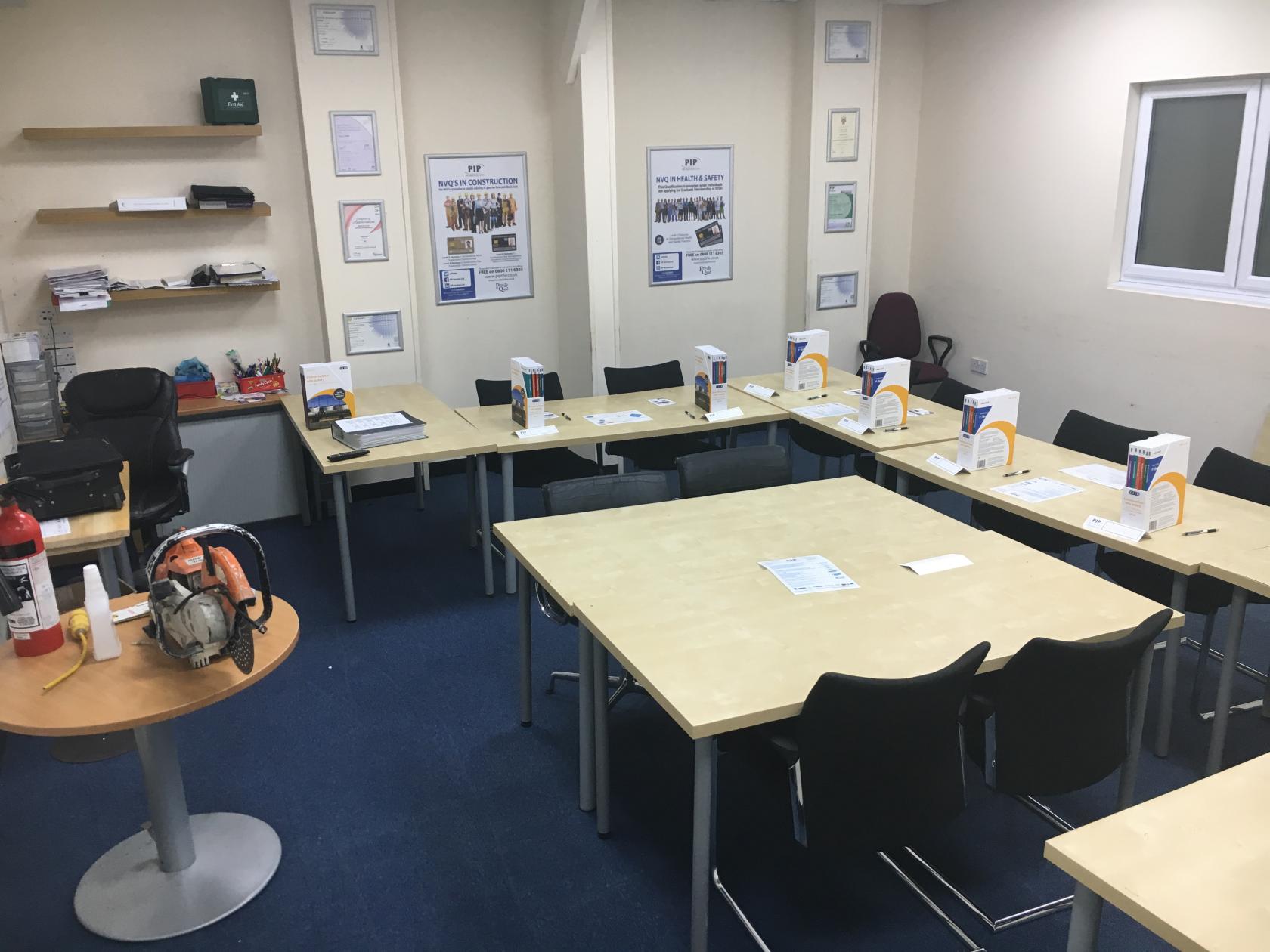 A training room with rectangular tables arranged in a U-shape, presentation materials, and blue carpet at PIP Services Ltd.