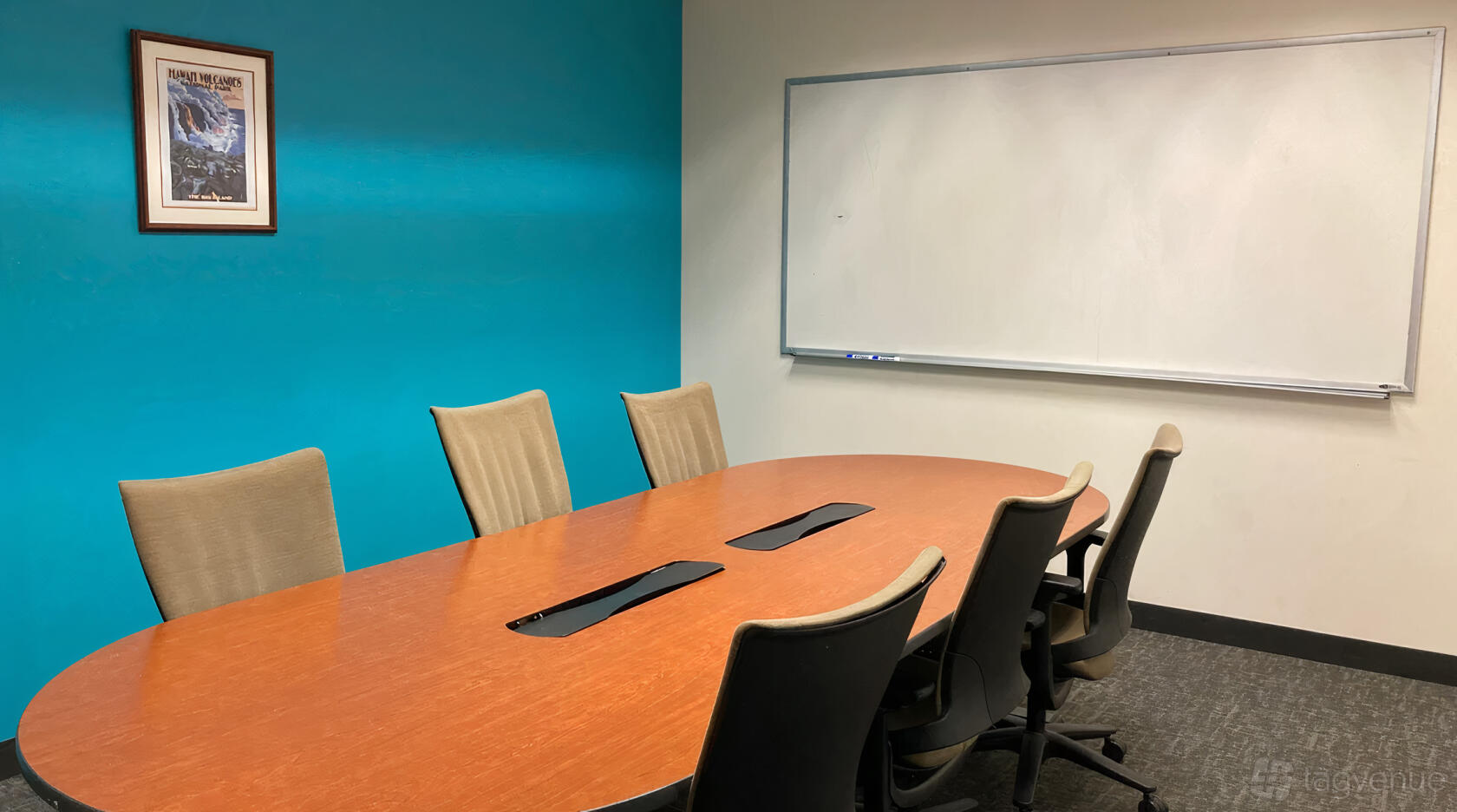 A coworking space with a long wooden conference table, tan chairs, blue accent wall, and whiteboard at SURF Incubator.