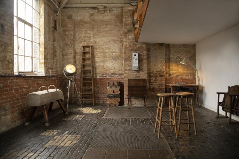 A photo studio with exposed brick walls, tall windows, vintage furniture, and industrial lighting at Espero Studio.