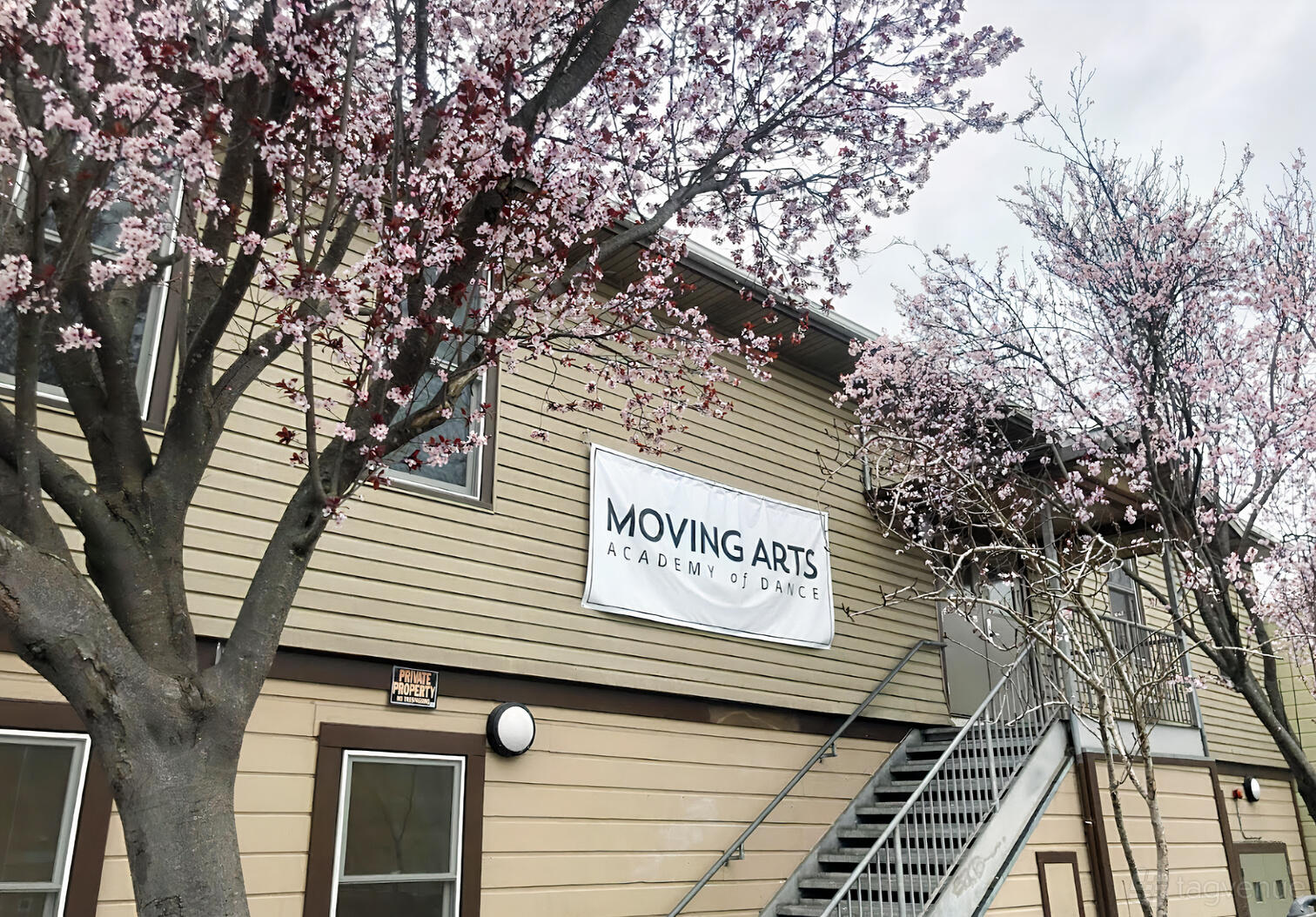 A dance studio with beige siding, exterior staircase, and blossoming trees at Moving Arts Academy of Dance.