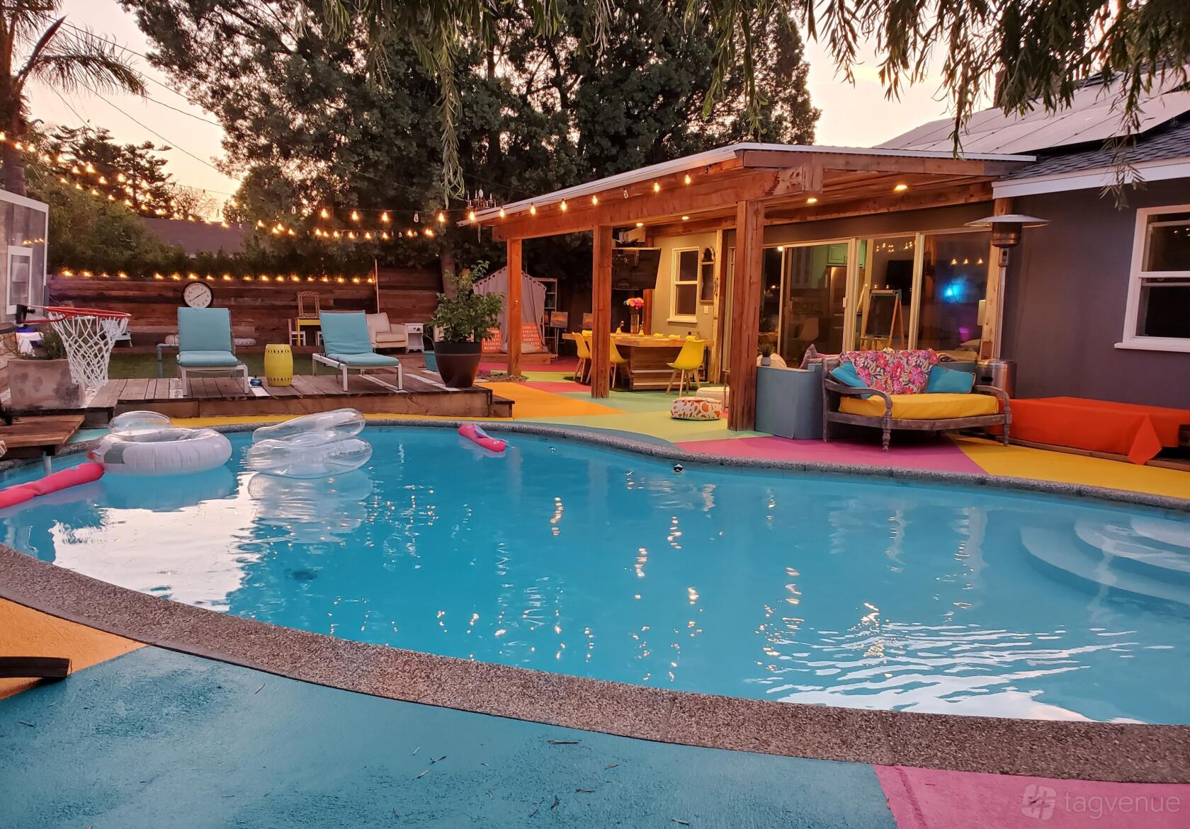 A house with a backyard pool, colorful patio seating, string lights, and inflatable pool floats at Dream Scape Oasis.