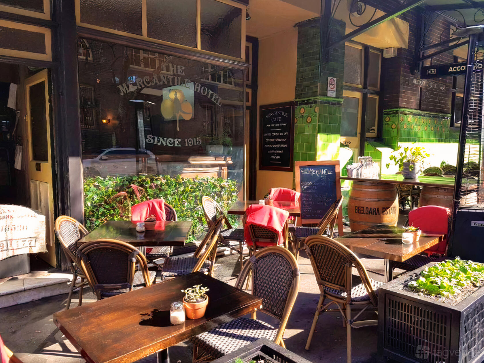 An outdoor seating area with wicker chairs, red tablecloths, and potted plants at The Mercantile Hotel.