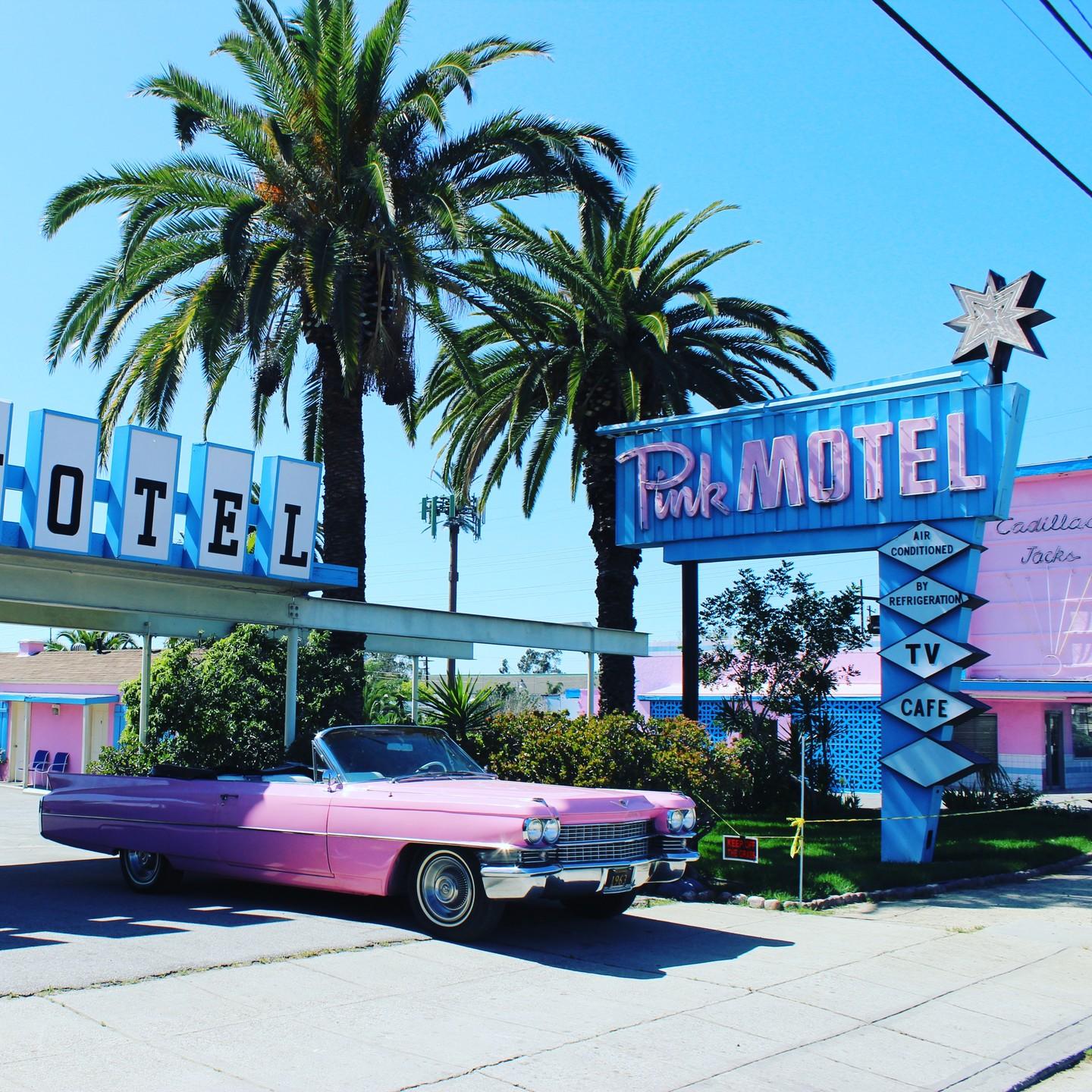 A vintage cafe with a retro pink motel sign, pink convertible, and palm trees at Pink motel/Pink Cafe.