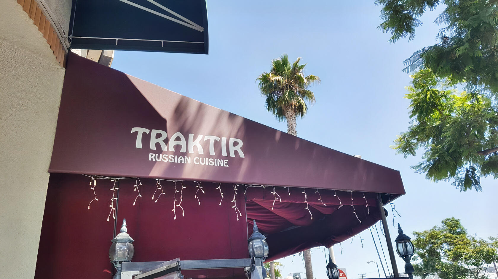 A restaurant entrance with a red awning labeled 'Traktir Russian Cuisine' and hanging string lights at Traktir Restaurant West Hollywood.