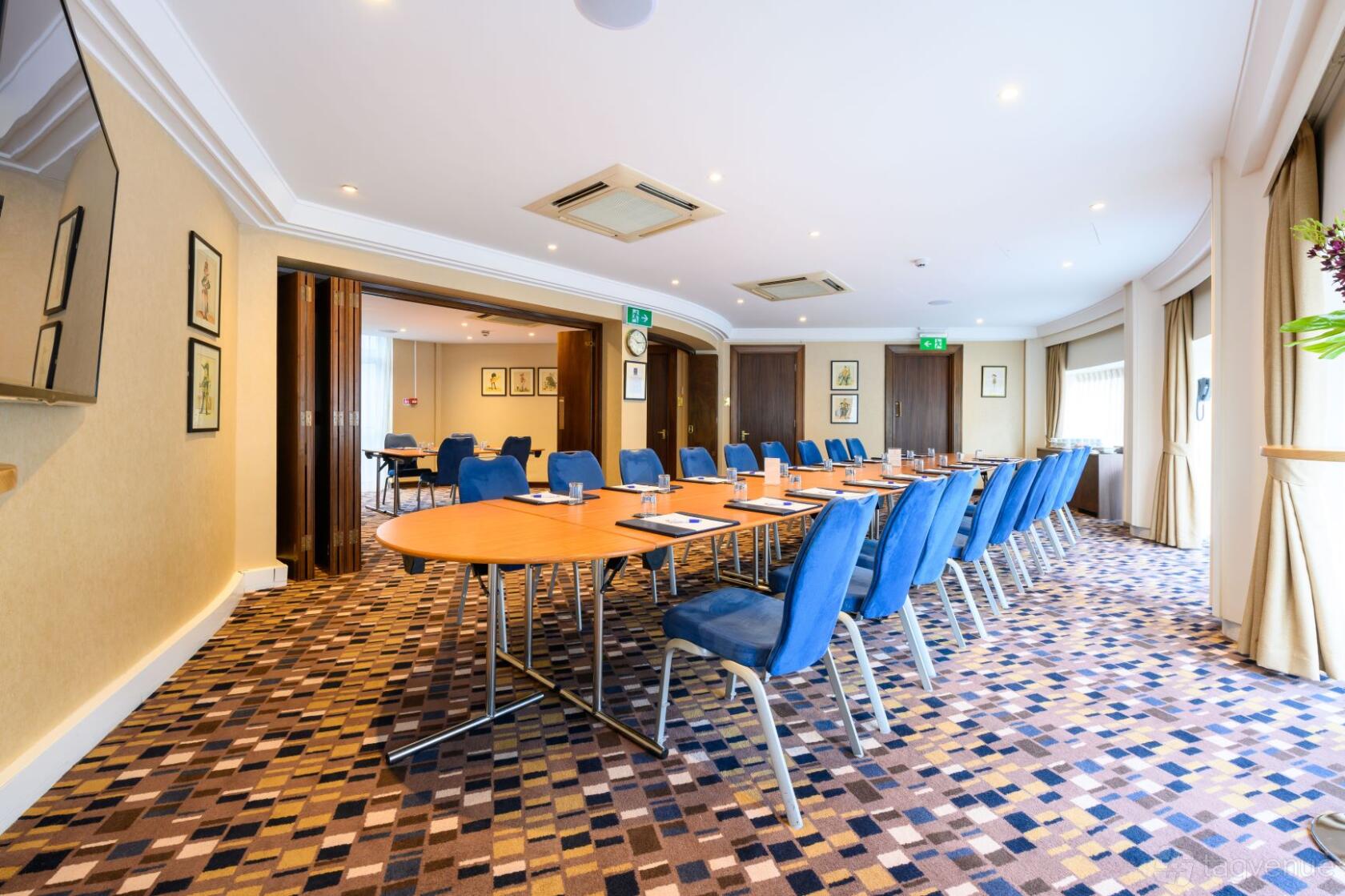 An event room with oval tables, blue cushioned chairs, large windows, and patterned carpet at Victory Services Club.