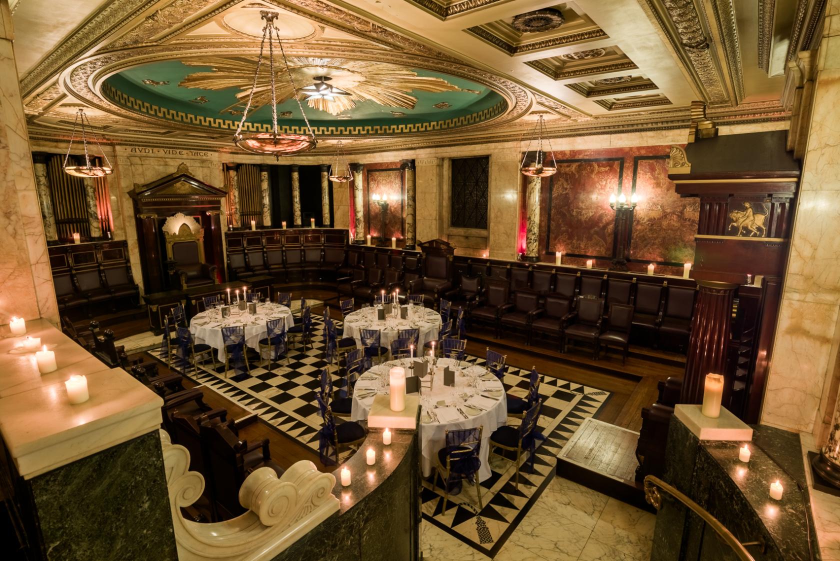A banqueting hall with marble walls, ornate ceiling, and round tables set on a checkered floor at Andaz London Hotel.