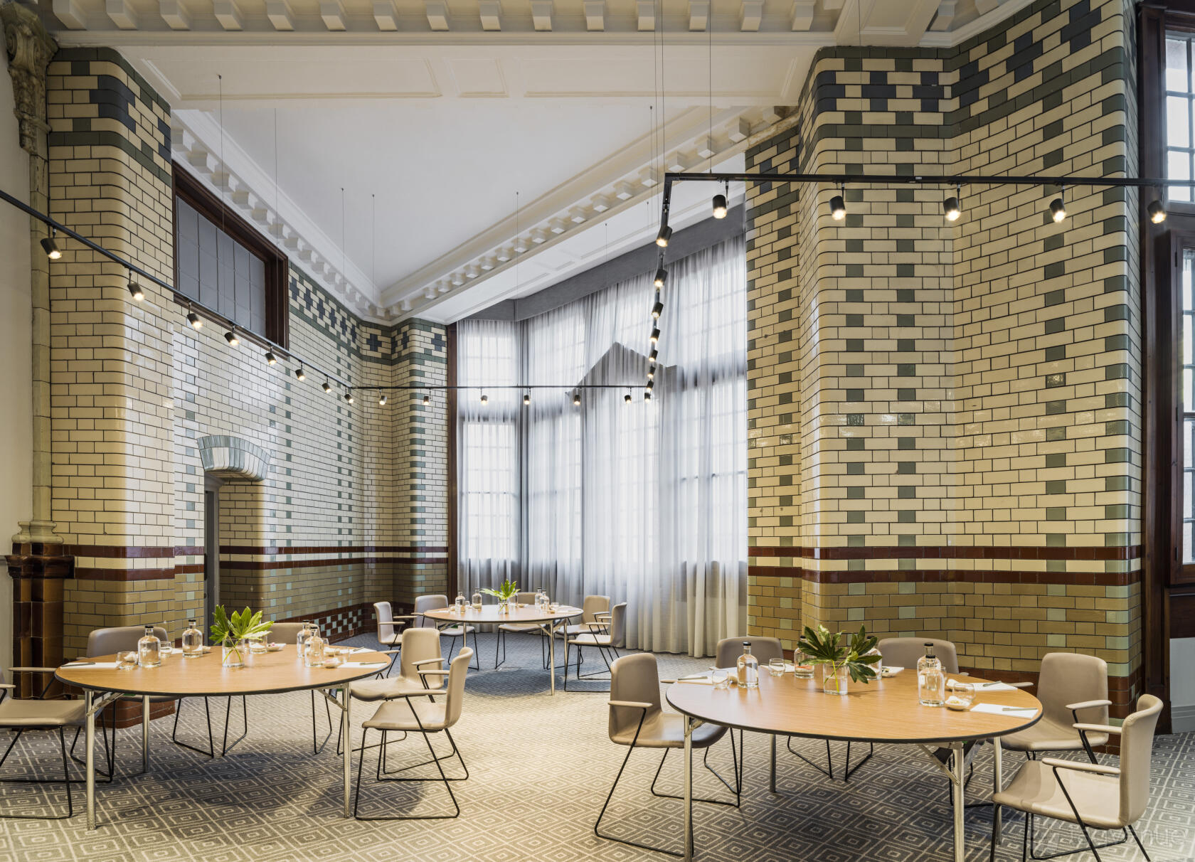 A hotel meeting room with high ceilings, exposed brick walls, tall windows, and round tables at Kimpton Clocktower Manchester.