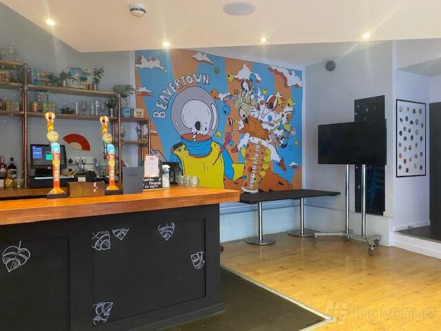 An event space in a pub with a colorful mural, wooden floors, and a bar counter at The Conductor.