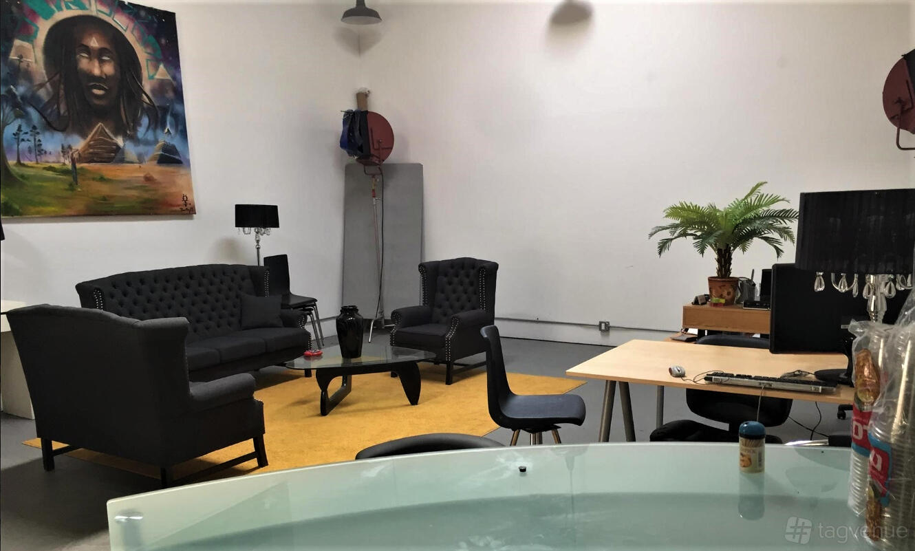 A coworking space with black tufted sofas, a desk with computers, and wall art at Hidden GEM Creative Studio.
