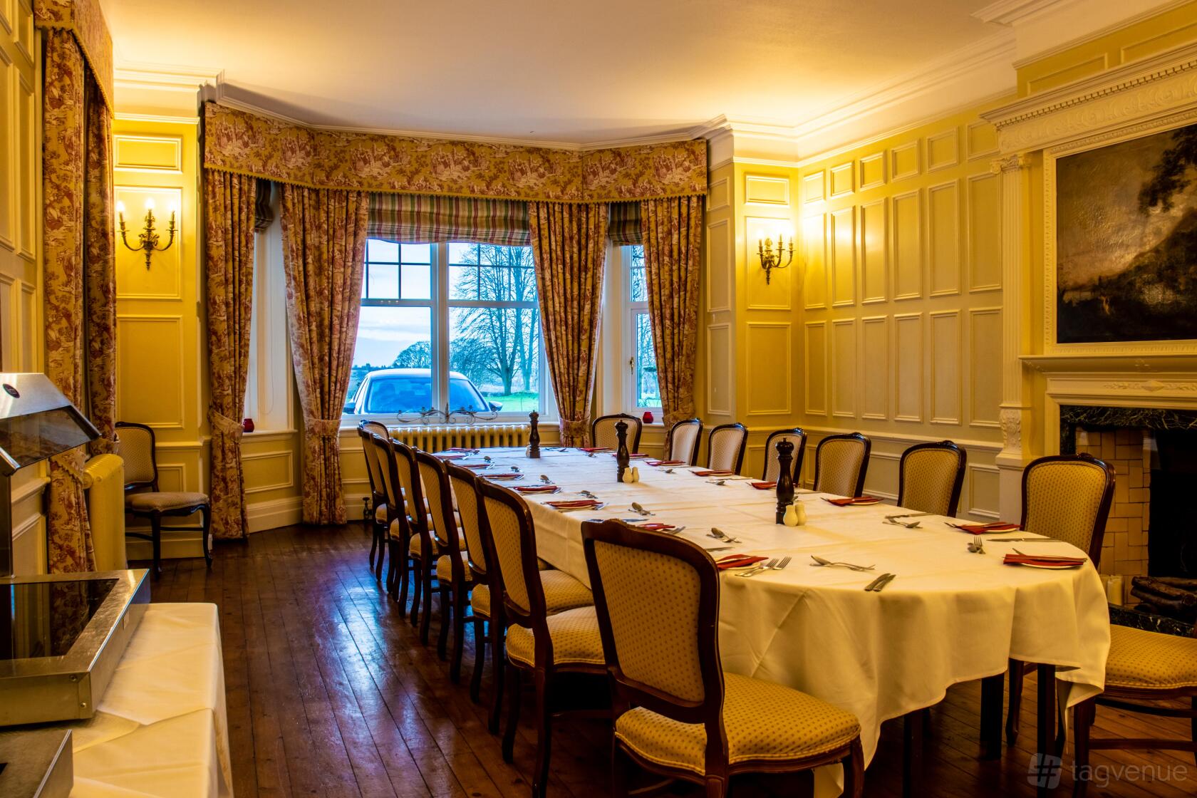 A country house dining room with a long table, upholstered chairs, wood floors, and large bay windows at Middle Aston House.