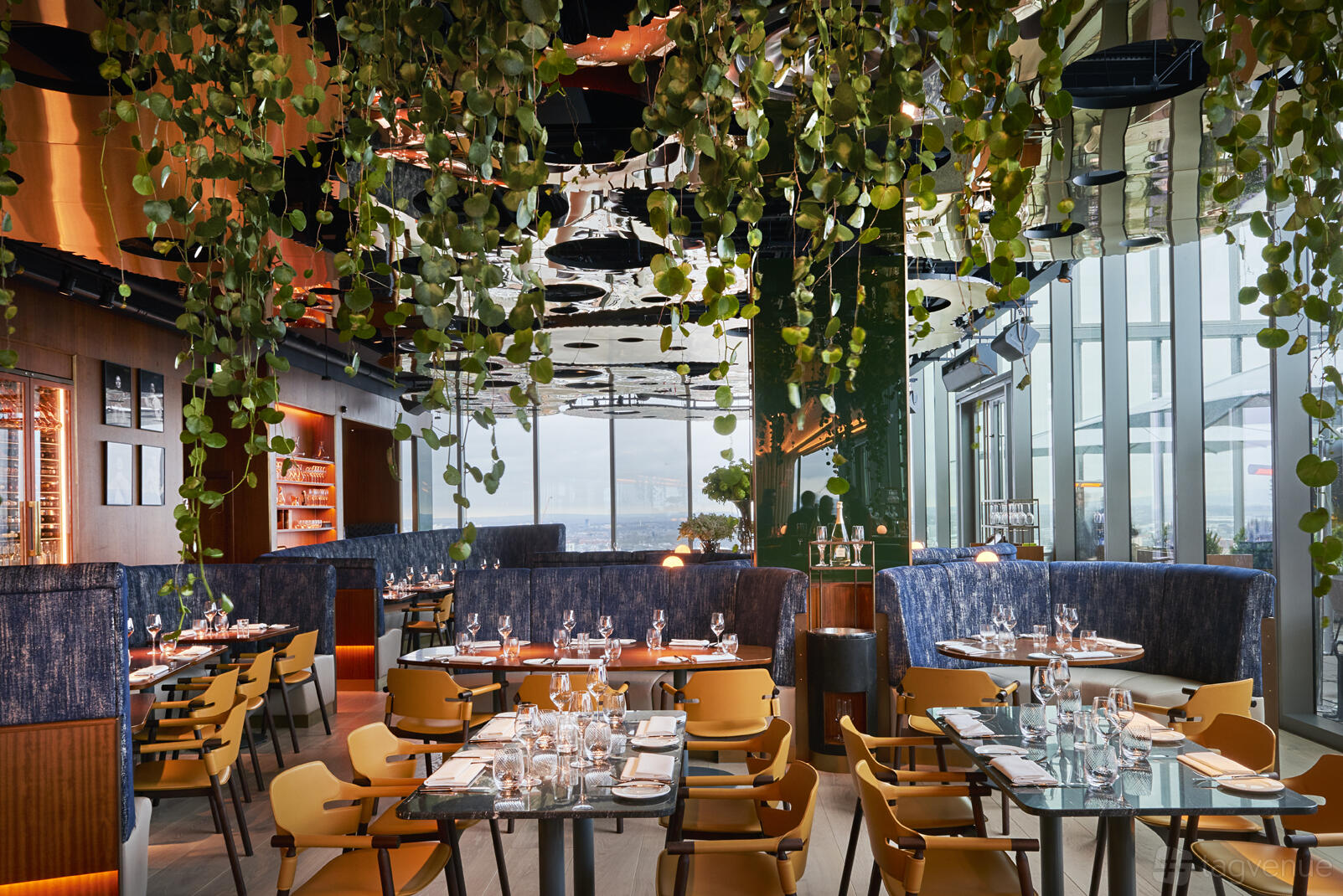 A restaurant with floor-to-ceiling windows, lush hanging greenery, and set tables with glassware at 20 Stories.