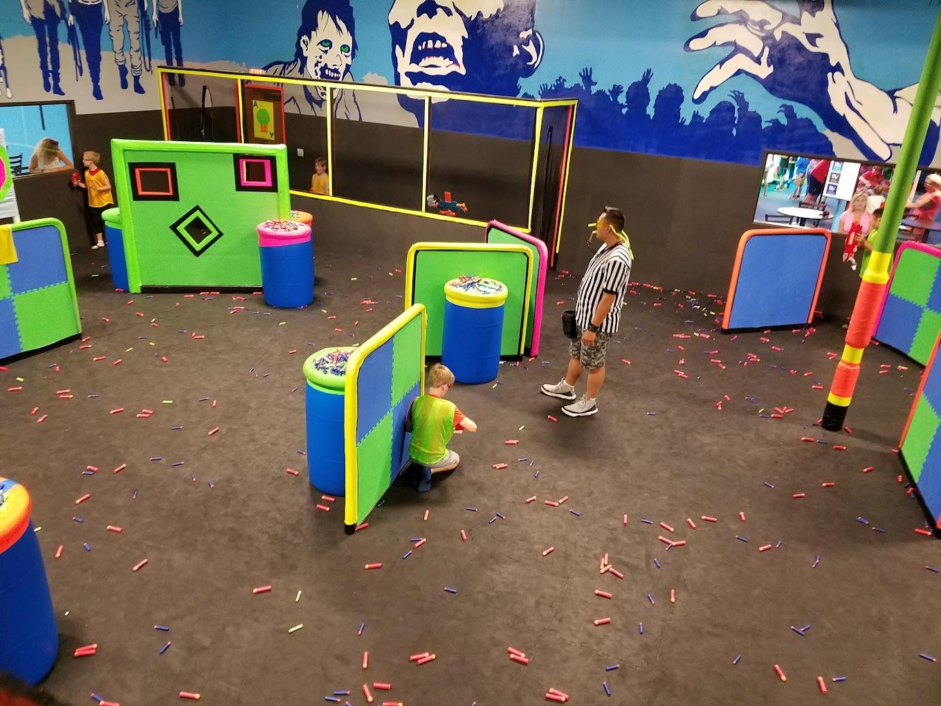 An event venue with neon-colored obstacles and scattered foam darts in the Nerf Arena at Dart'em Up.