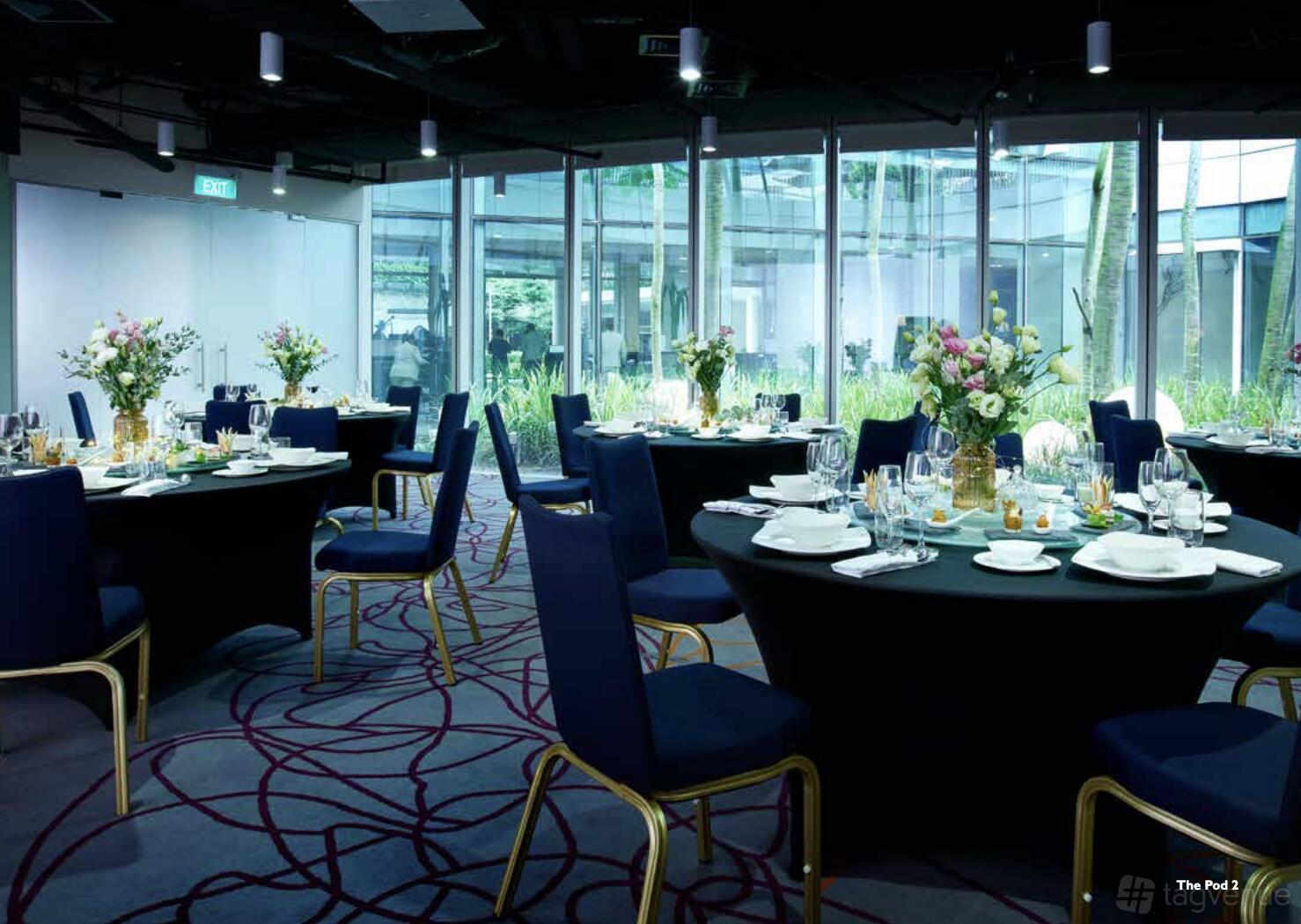 A hotel meeting room with round tables, navy chairs, floral centerpieces, and floor-to-ceiling windows at Capri Changi City.