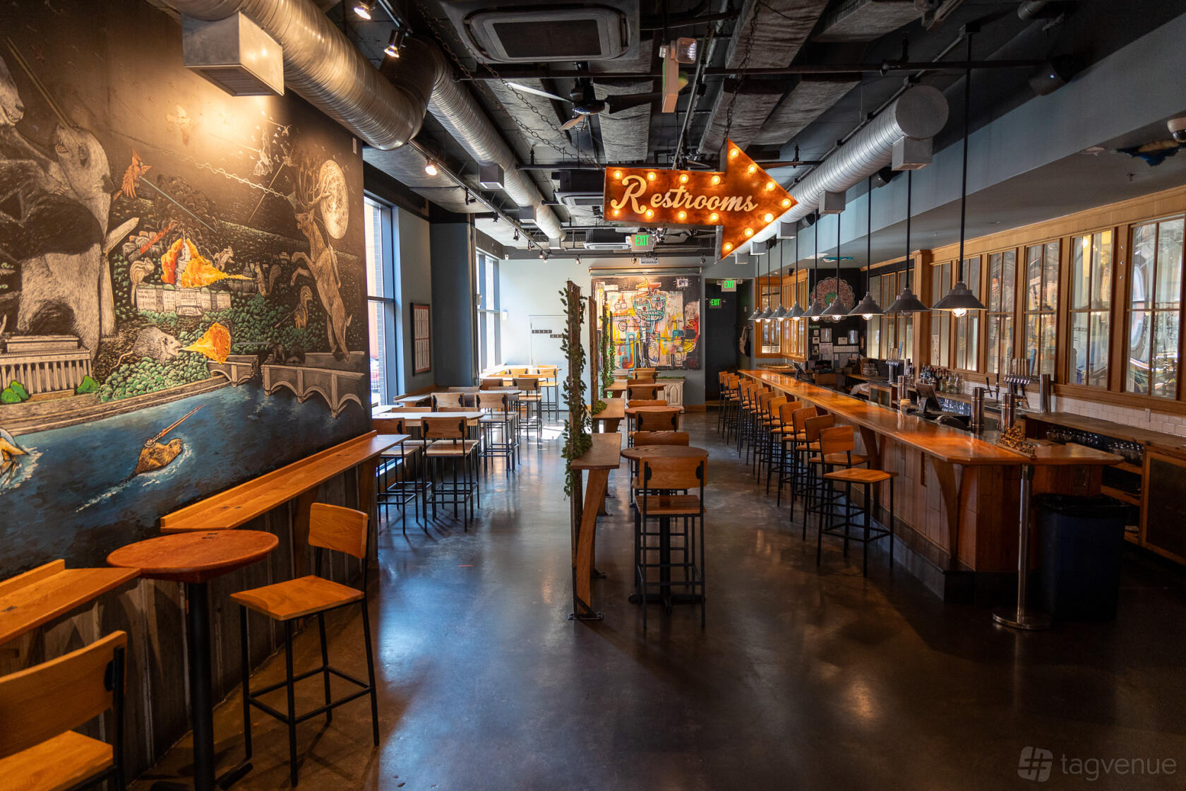 A restaurant with mural-covered walls, wood tables, and a long bar with pendant lighting at Right Proper Brewing Company.