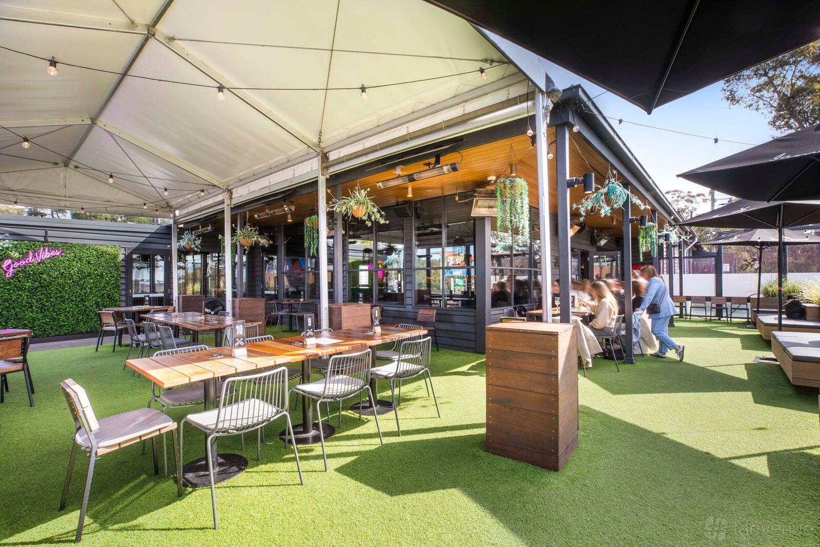 An outdoor pub space with artificial grass, wooden tables, metal chairs, and hanging plants at The Rogue Squire.