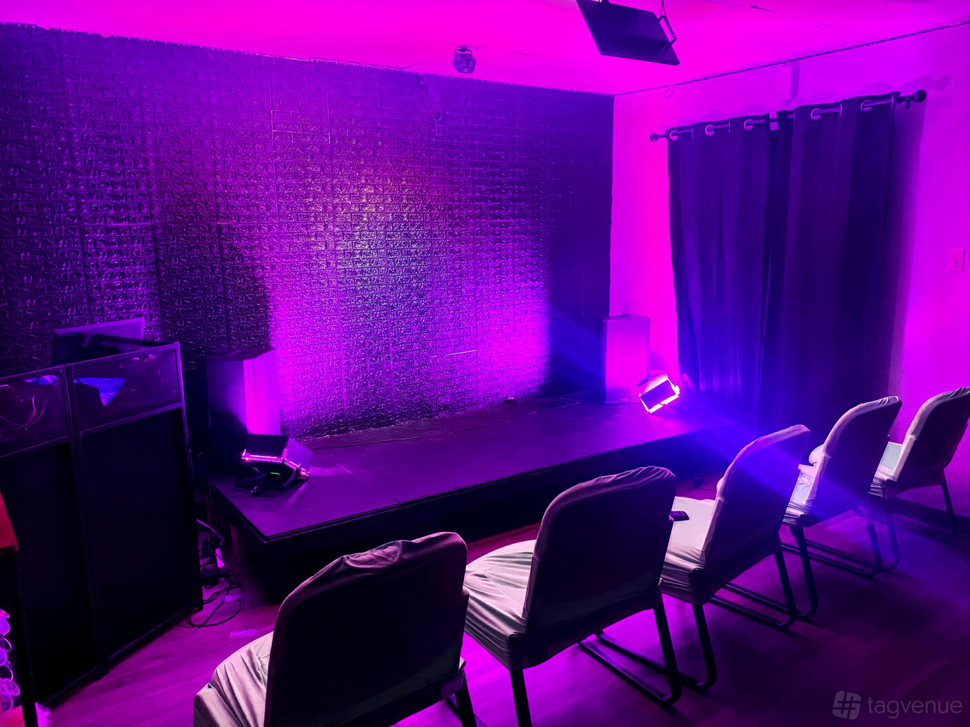 An event space in a recording studio with a small stage, acoustic panel wall, purple lighting, and rows of chairs at Vibe Lab LLC.