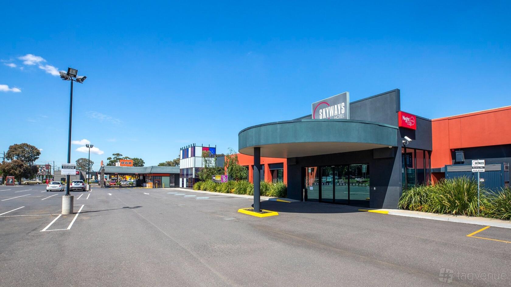A hotel exterior with a covered entrance, glass doors, and parking lot at Skyways Hotel.
