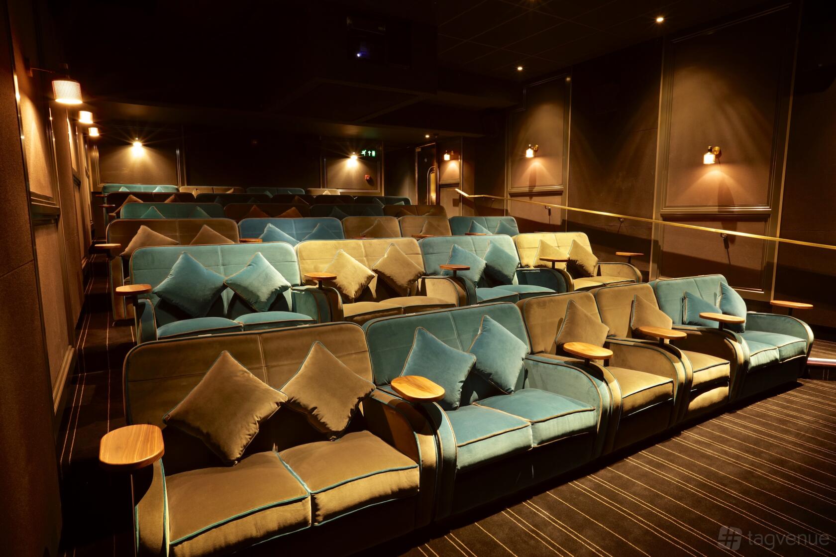 An auditorium with plush velvet armchairs, small wooden tray tables, and ambient wall lighting at Everyman Oxted.