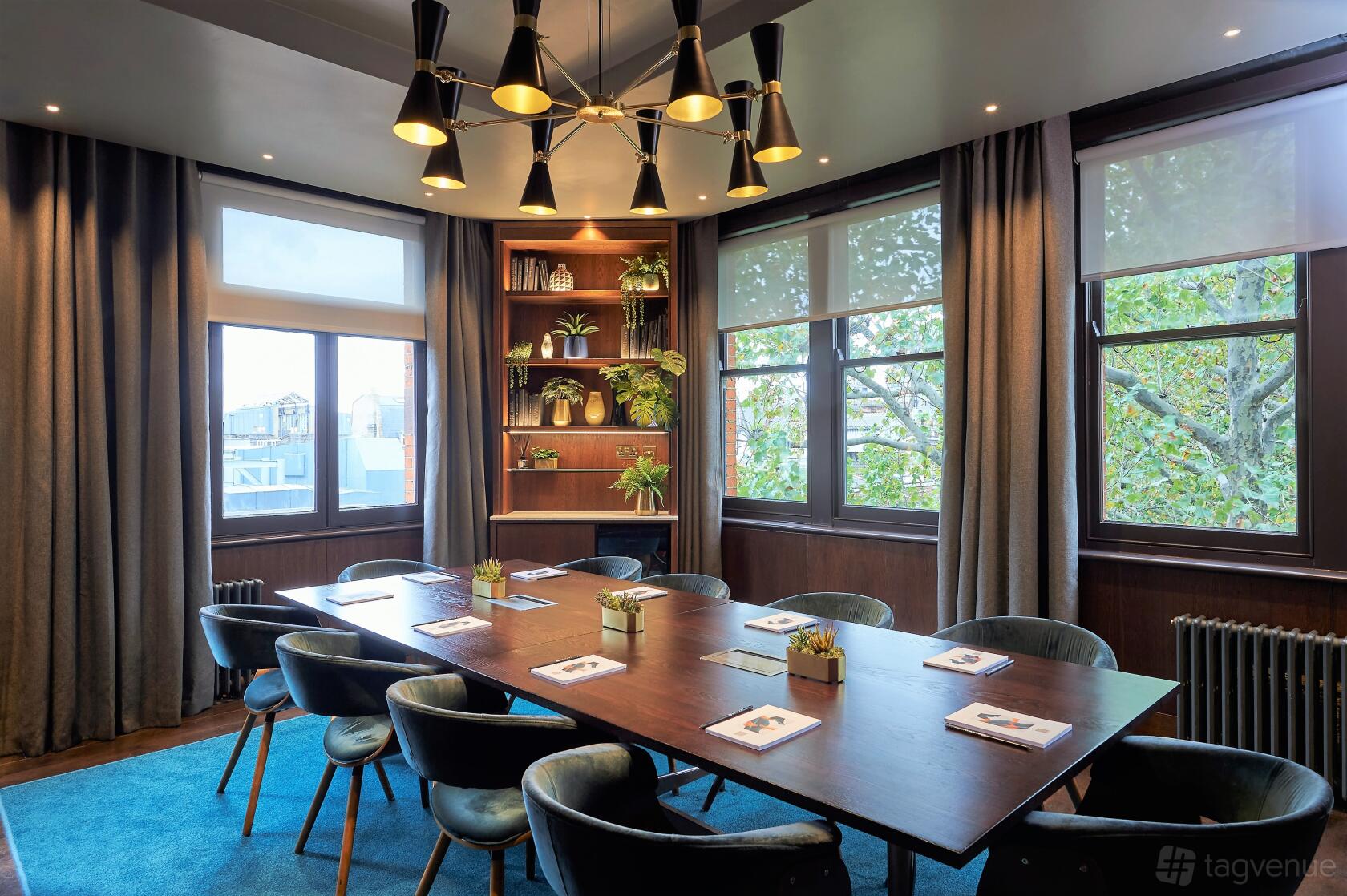 A bar meeting room with large windows, a wooden table surrounded by velvet chairs, and potted plants at Century Club.
