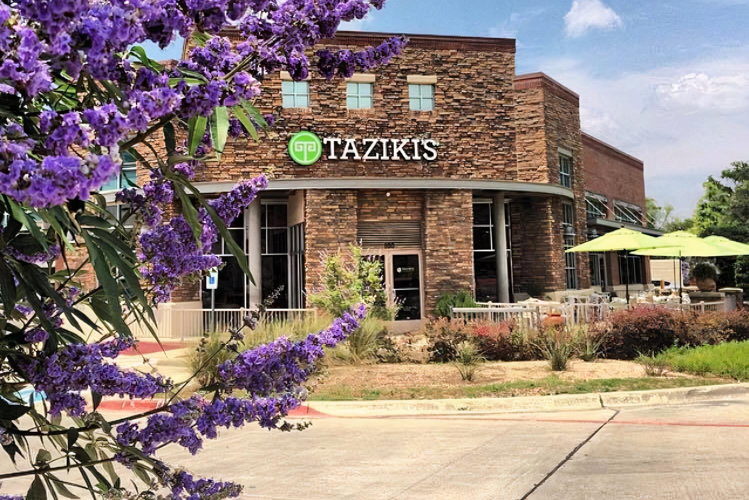 A restaurant with a stone façade, large windows, and a patio area with green umbrellas at Taziki's Mediterranean Cafe Southlake.