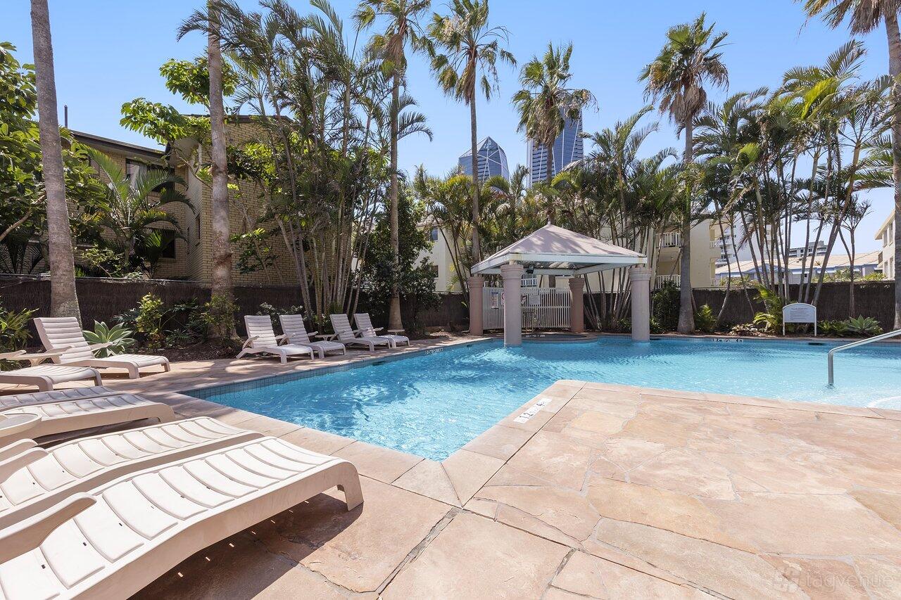 An outdoor hotel pool with lounge chairs, a poolside cabana, and palm trees at Oaks Gold Coast Hotel.