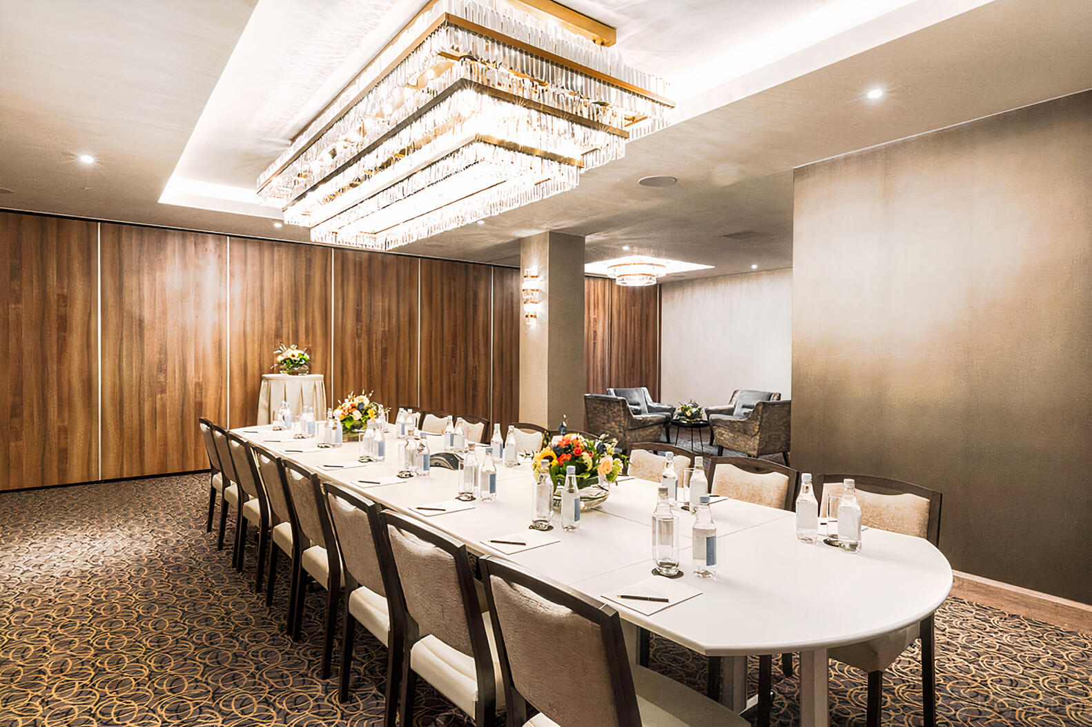 An event space with a long white conference table, upholstered chairs, and crystal chandeliers at The Royal London Suites.