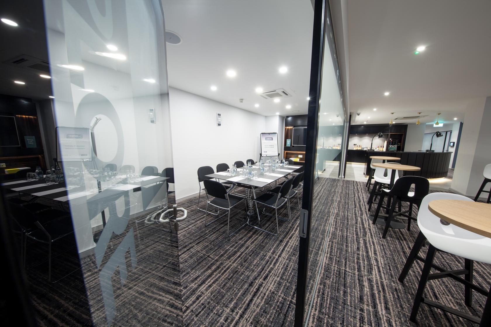 A meeting room with glass walls, conference table, black chairs, and water glasses at The BCEC.