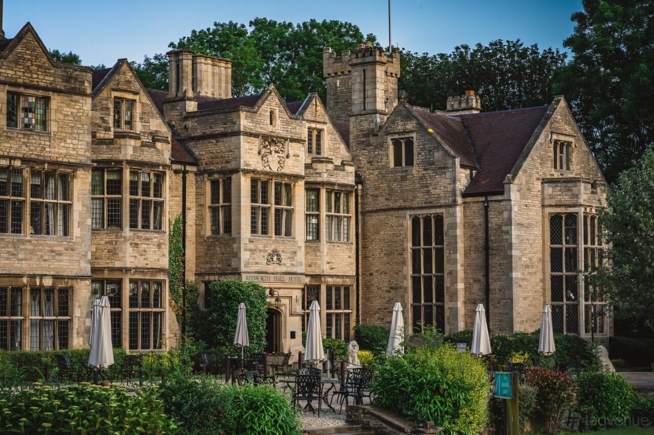 A historic hotel with stone façade, tall windows, and an outdoor terrace with patio tables and umbrellas at Redworth Hall Hotel.