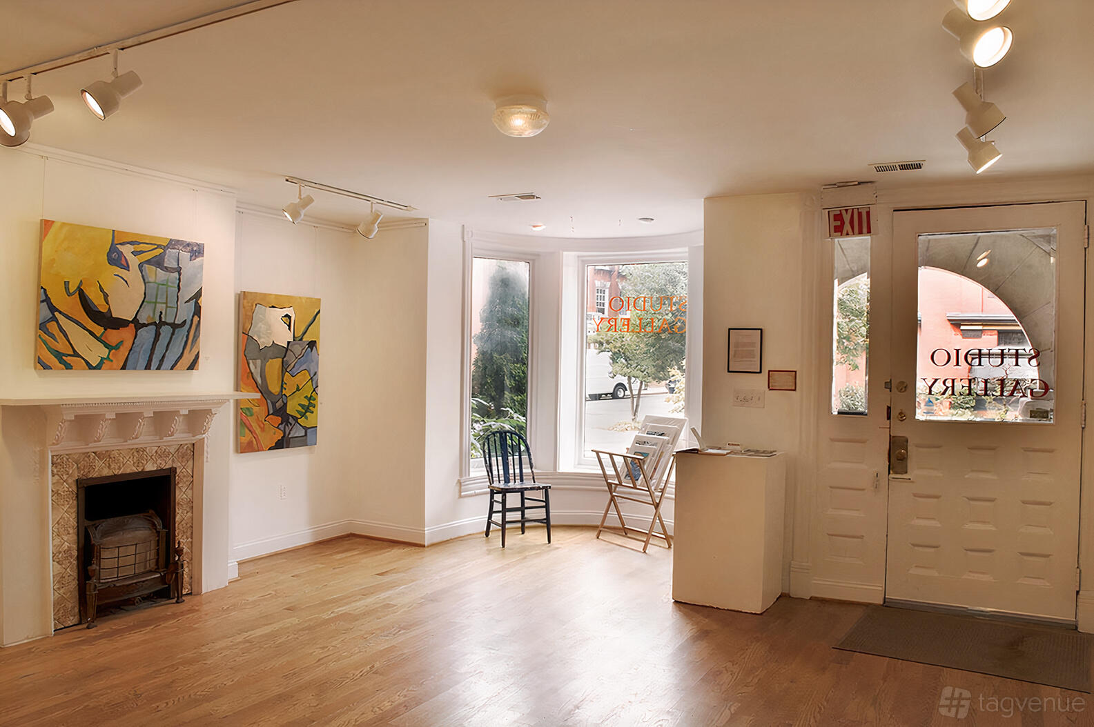 A gallery with hardwood floors, white walls, colorful artwork, and large front windows at Studio Gallery.