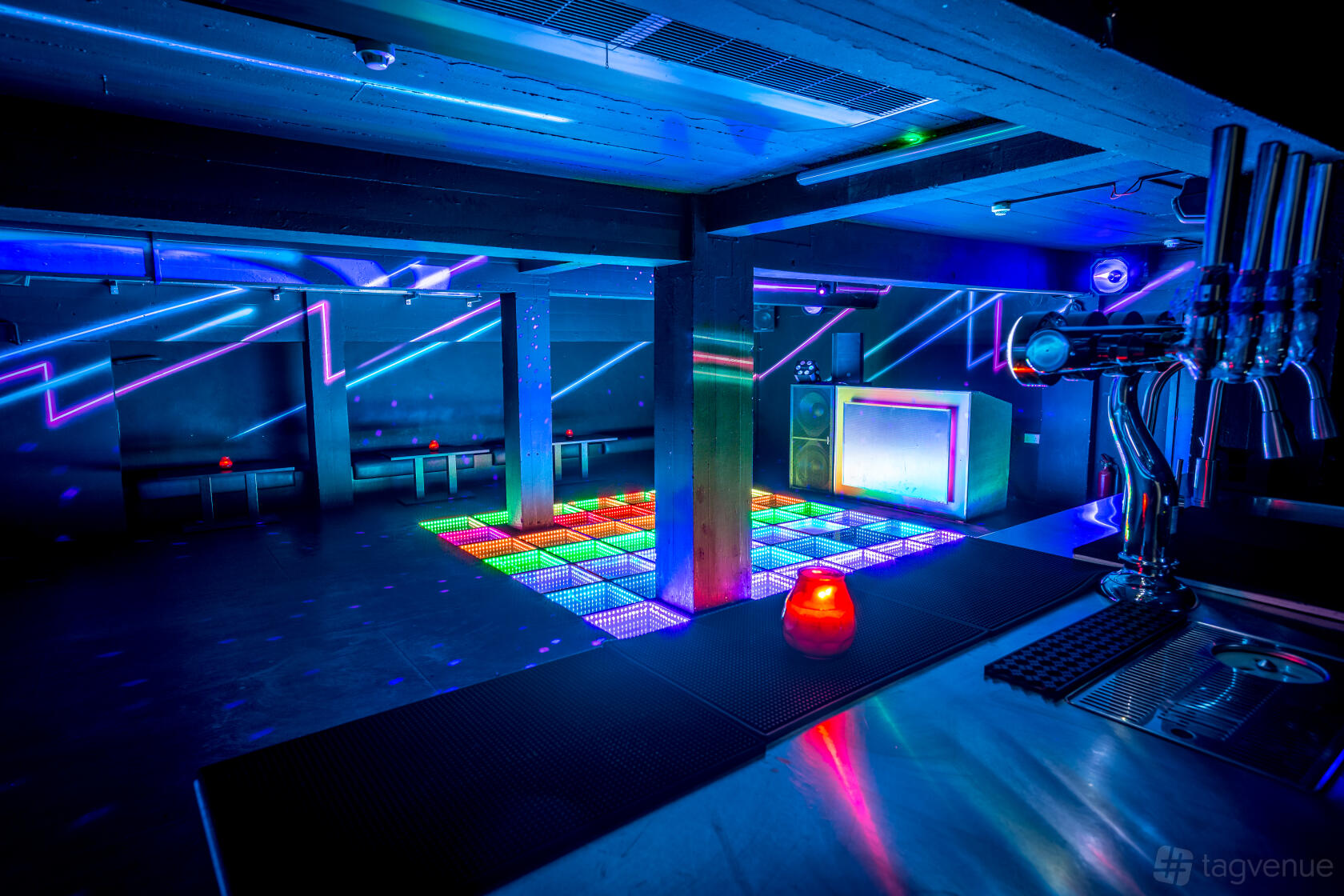 An event space in a nightclub with LED dance floor, neon wall lights, and a bar counter at Queen of Hoxton.