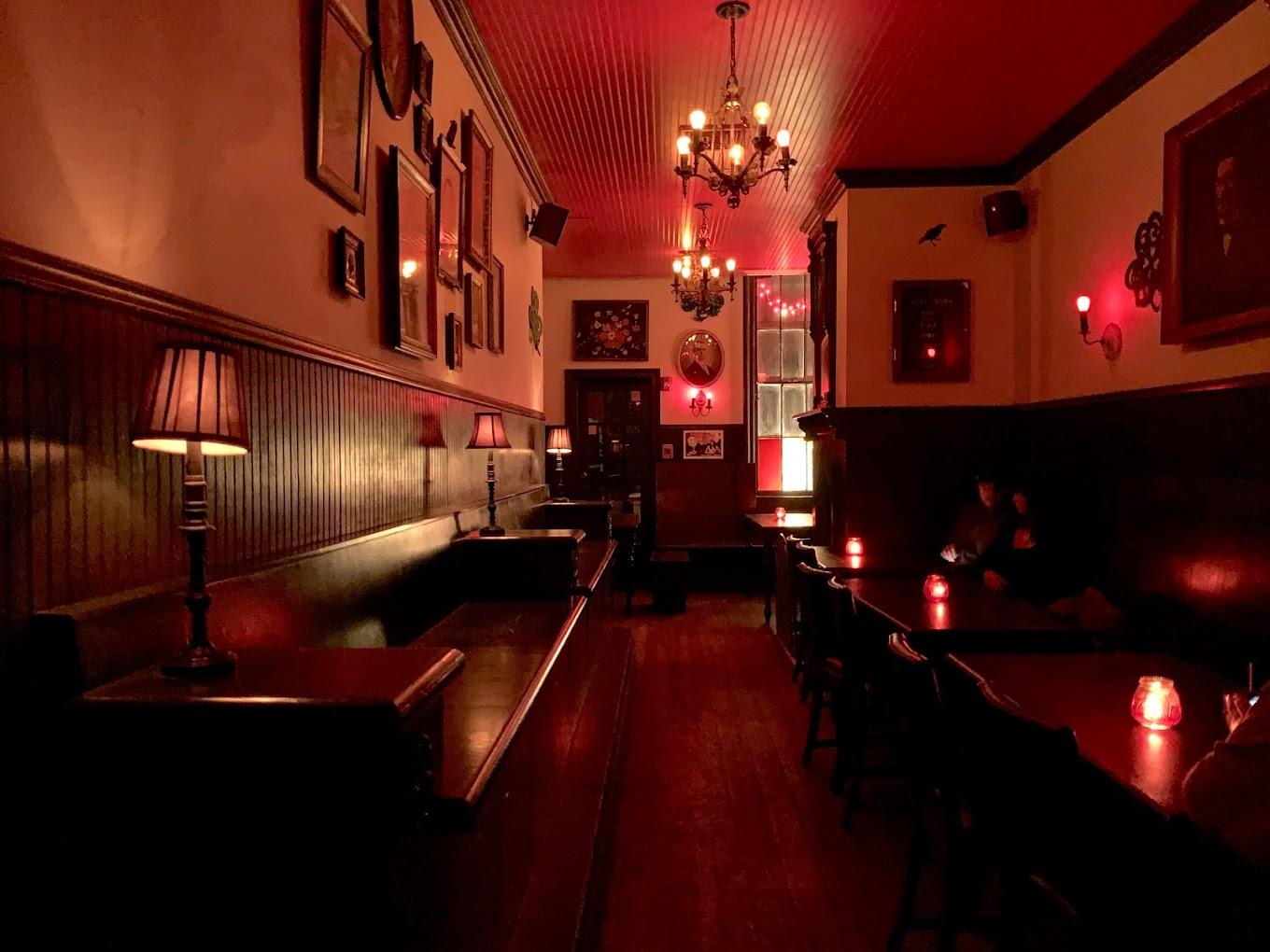 A dimly lit bar with dark wood paneling, red ceiling, chandeliers, and framed wall art at Black Rabbit.