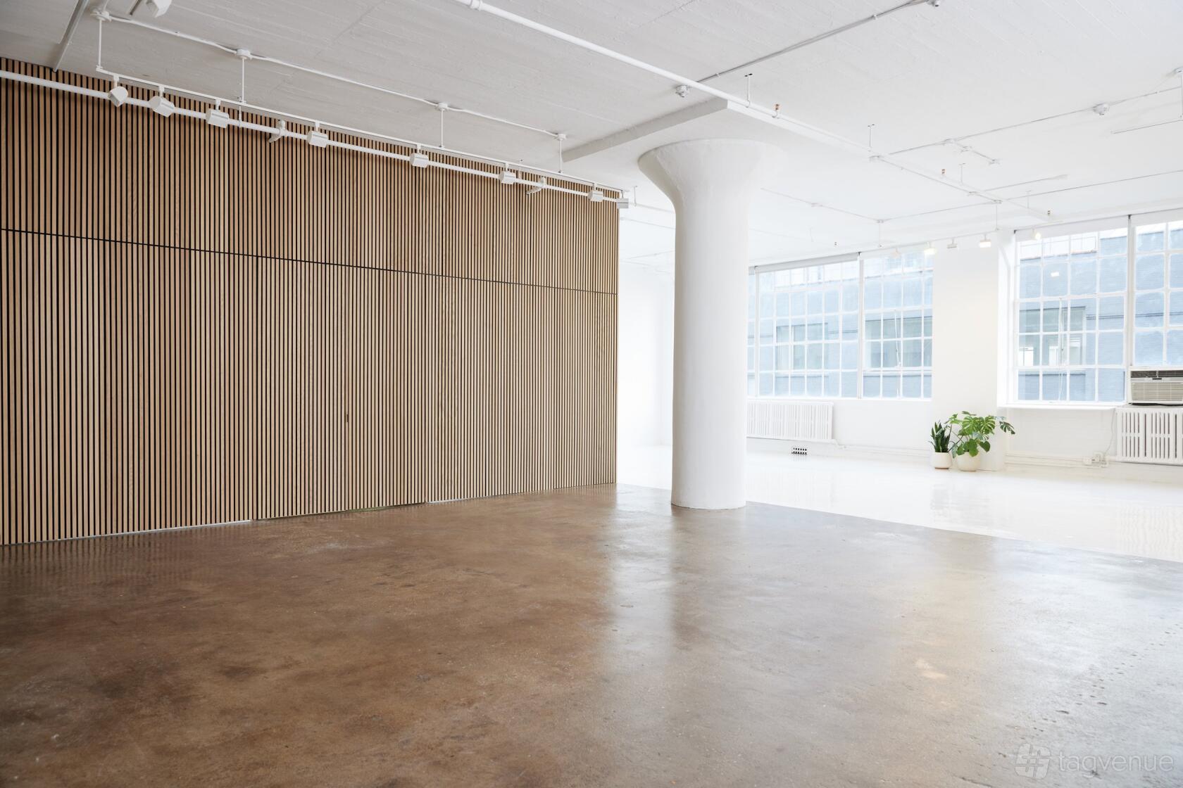 An event venue with polished concrete floors, slatted wood panel wall, and large factory windows at EDEN STUDIO NYC.